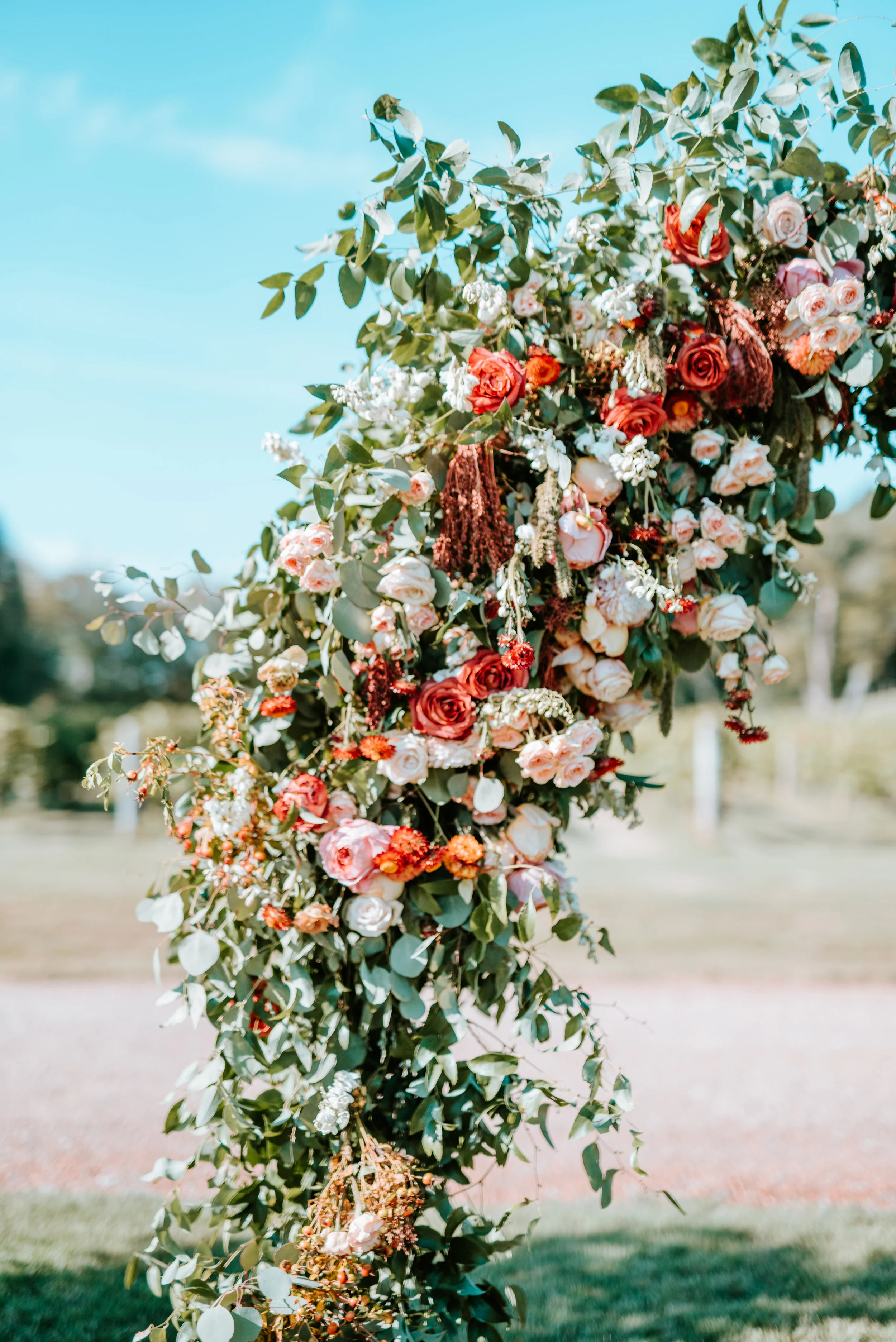 Lush floral arch for a fall wedding at Long Hollow Gardens with untamed greenery, berries, and rust orange garden roses.