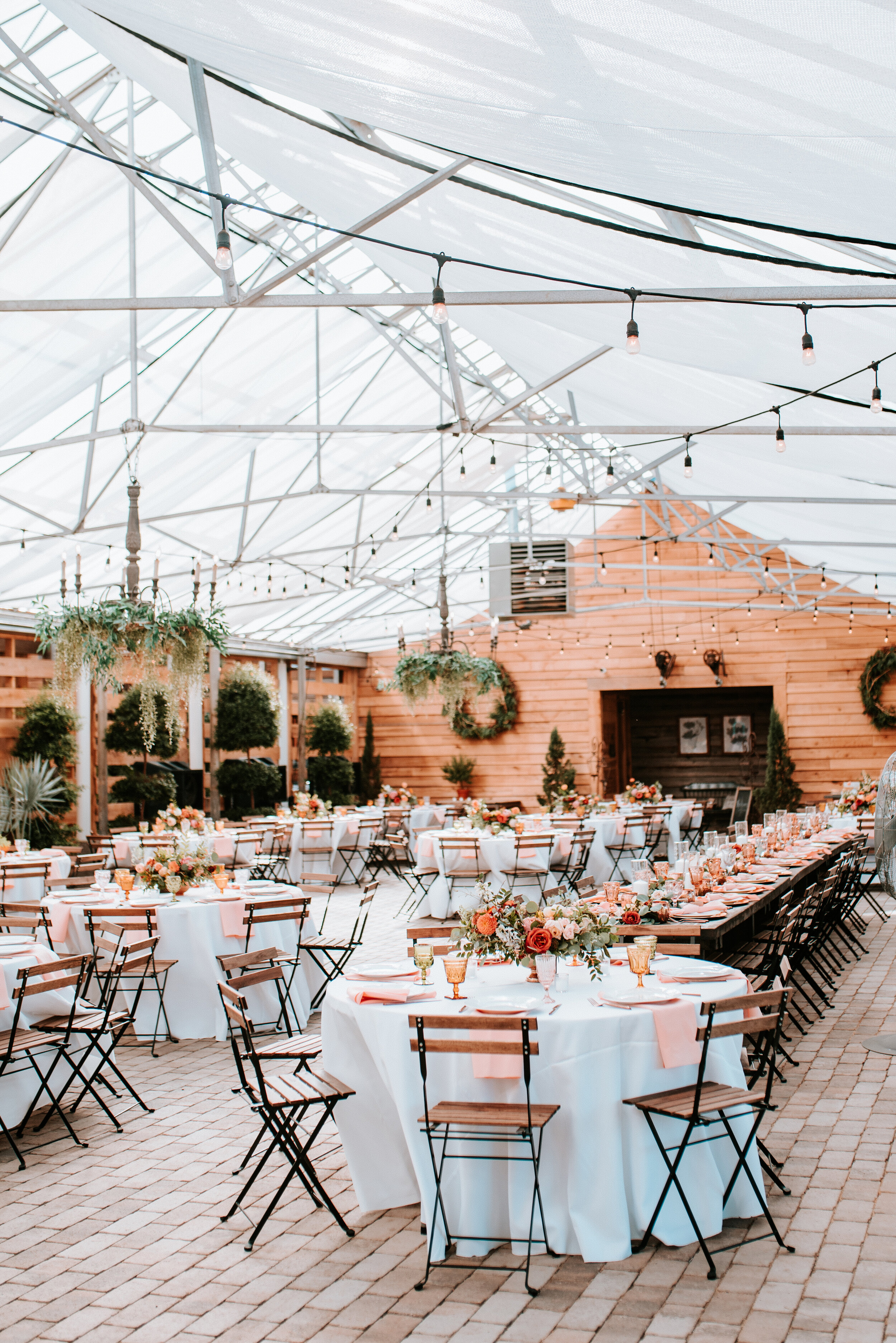 Greenhouse wedding reception with orange and peach flower arrangements of garden roses, ranunculus, berries, and wildflowers with asymmetrical, trailing greenery. Nashville wedding floral design.