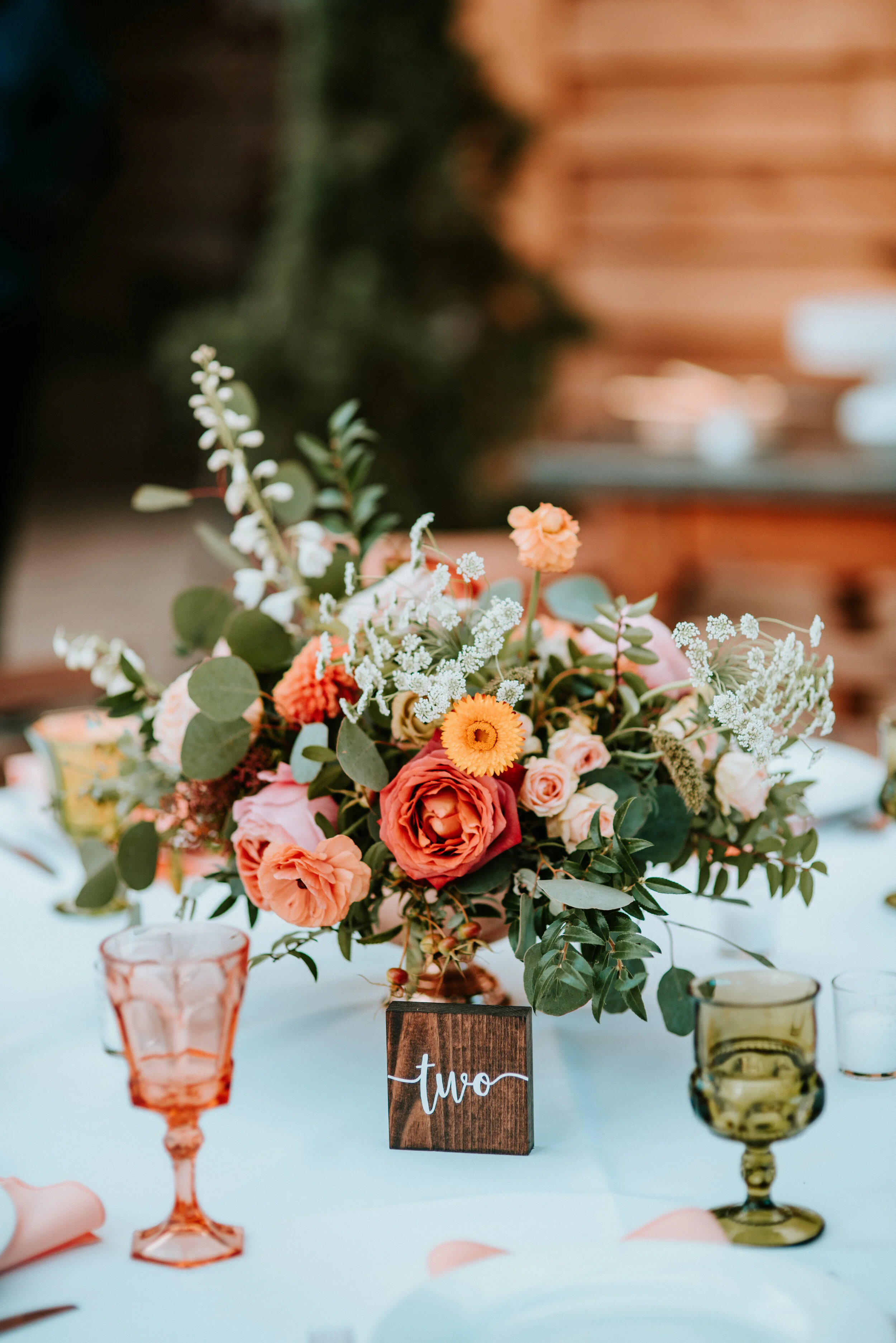 Greenhouse wedding reception with orange and peach flower arrangements of garden roses, ranunculus, berries, and wildflowers with asymmetrical, trailing greenery. Nashville wedding floral design.