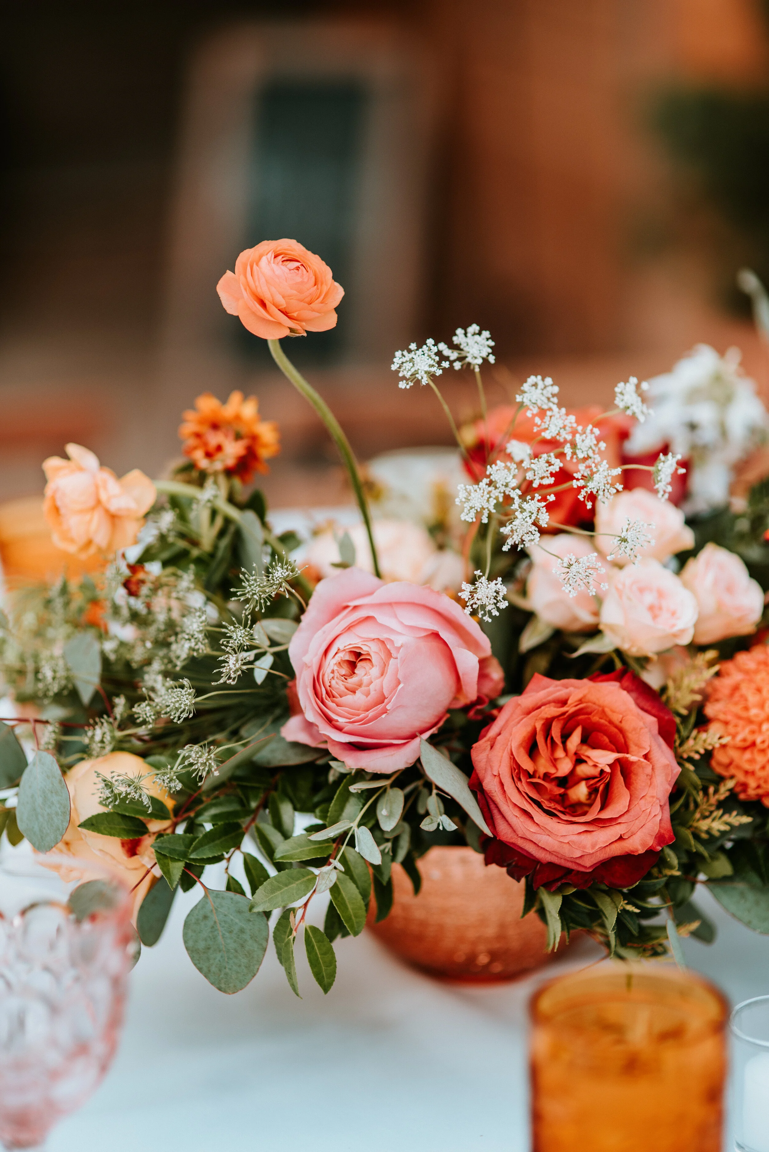 Greenhouse wedding reception with orange and peach flower arrangements of garden roses, ranunculus, berries, and wildflowers with asymmetrical, trailing greenery. Nashville wedding floral design.