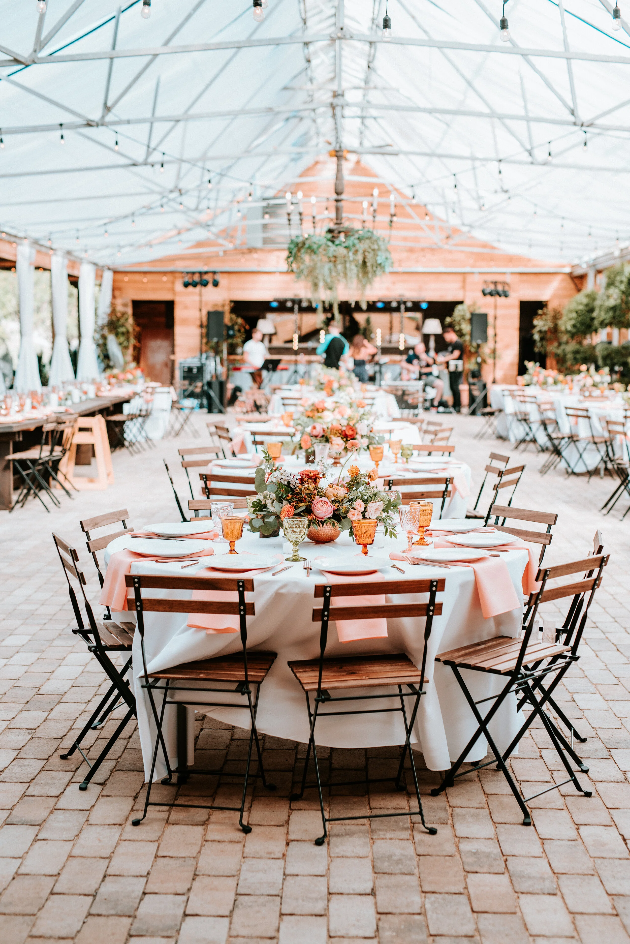 Greenhouse wedding reception with orange and peach flower arrangements of garden roses, ranunculus, berries, and wildflowers with asymmetrical, trailing greenery. Nashville wedding floral design.