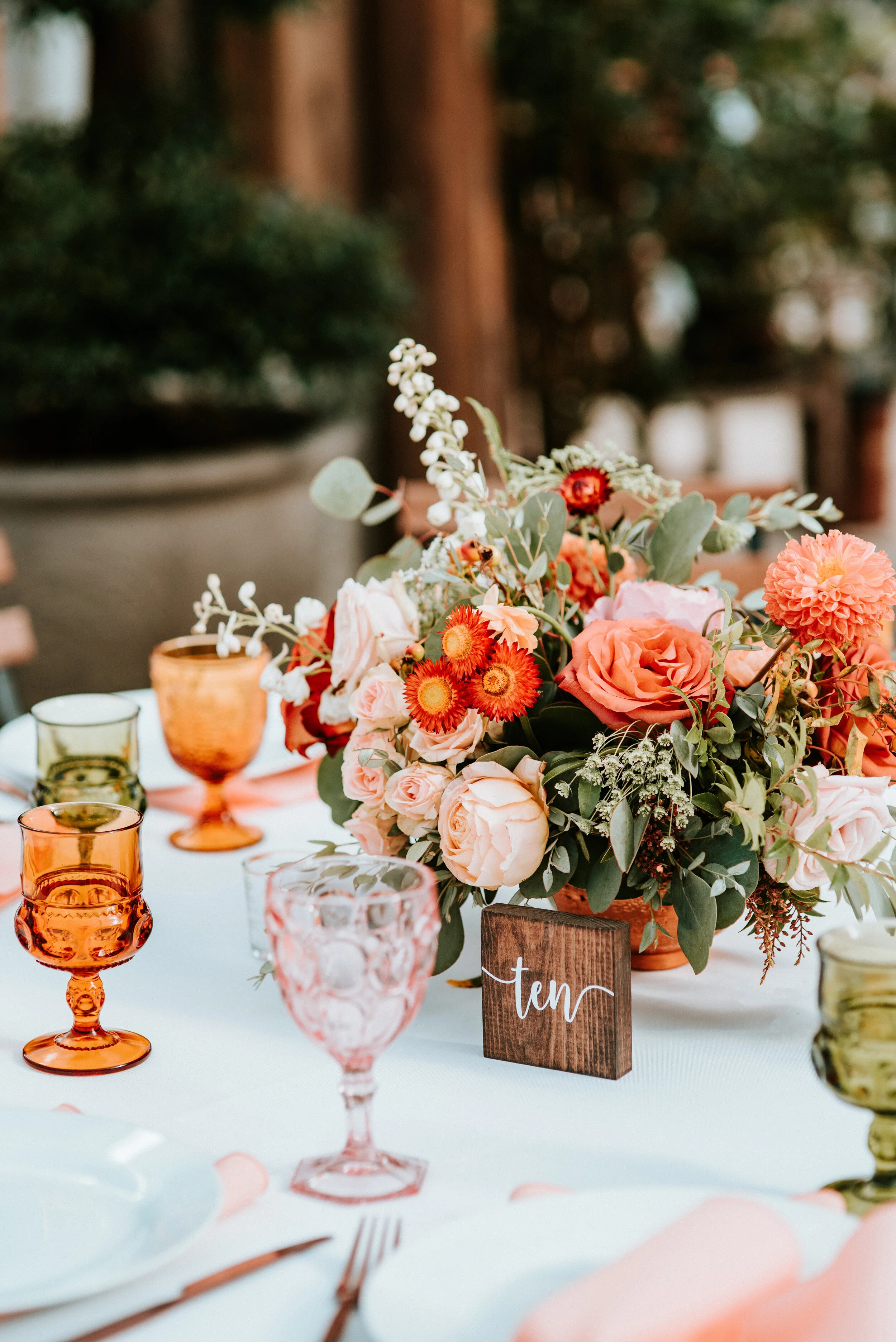 Greenhouse wedding reception with orange and peach flower arrangements of garden roses, ranunculus, berries, and wildflowers with asymmetrical, trailing greenery. Nashville wedding floral design.