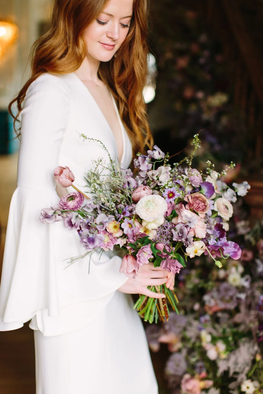 Whimsical purple bridal bouquet with delicate spring flowers like spirea, ranunculus, sweet peas, and tulips.