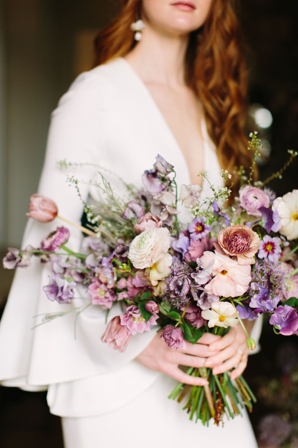 Whimsical purple bridal bouquet with delicate spring flowers like spirea, ranunculus, sweet peas, and tulips.