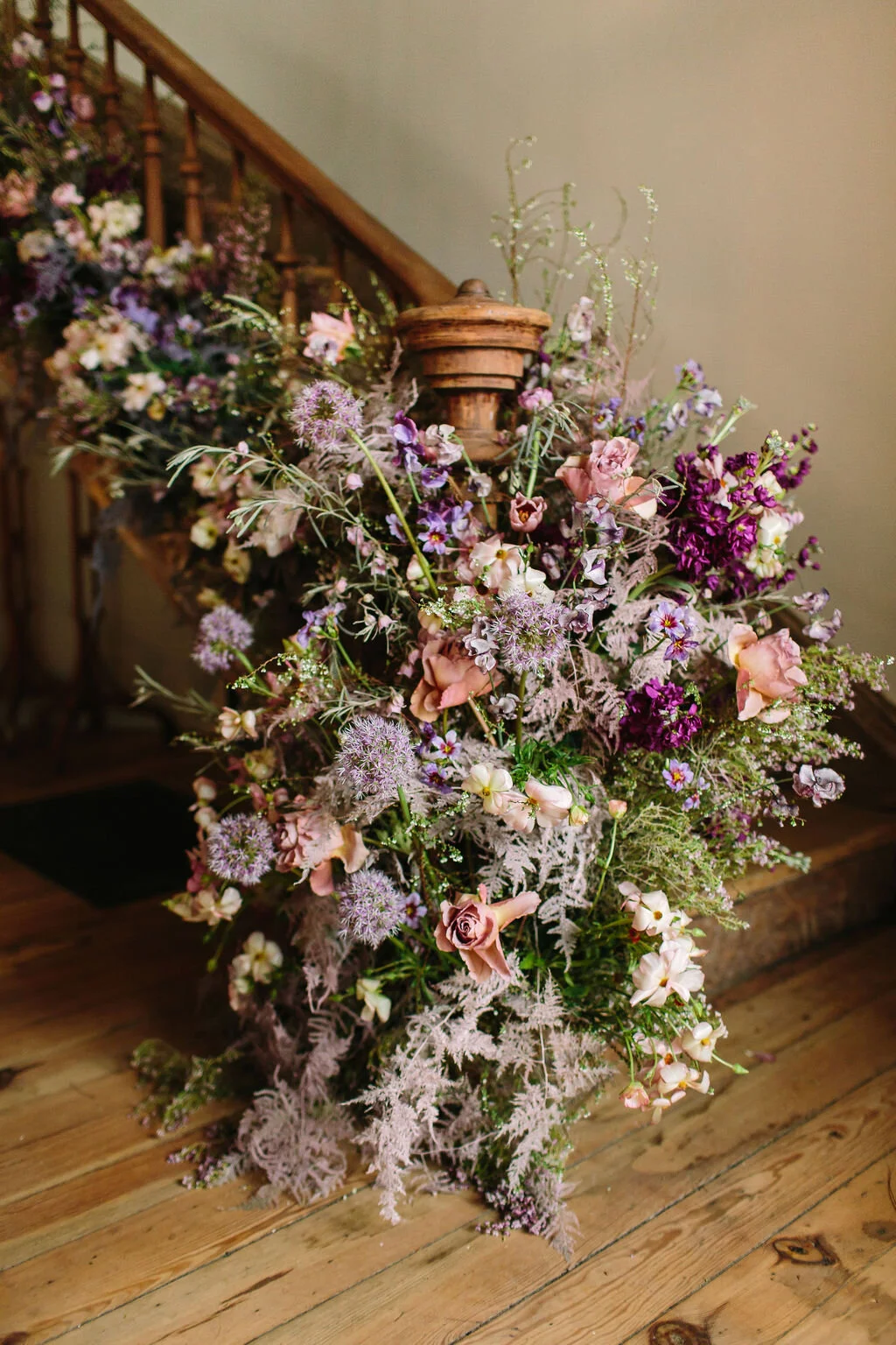 Spiral staircase with a lush, airy floral installation in a lavender and lilac color palette with spirea, painted plumosa ferns, heather, allium, ranunculus, and garden roses. Nashville Wedding Floral Design.