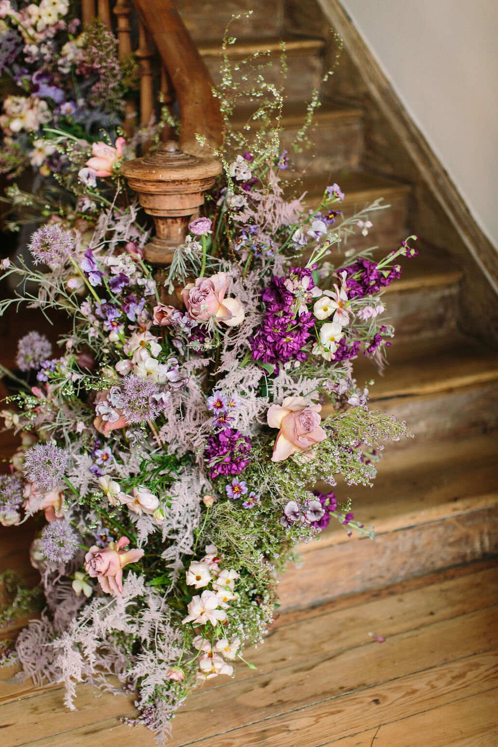 Spiral staircase with a lush, airy floral installation in a lavender and lilac color palette with spirea, painted plumosa ferns, heather, allium, ranunculus, and garden roses. Nashville Wedding Floral Design.