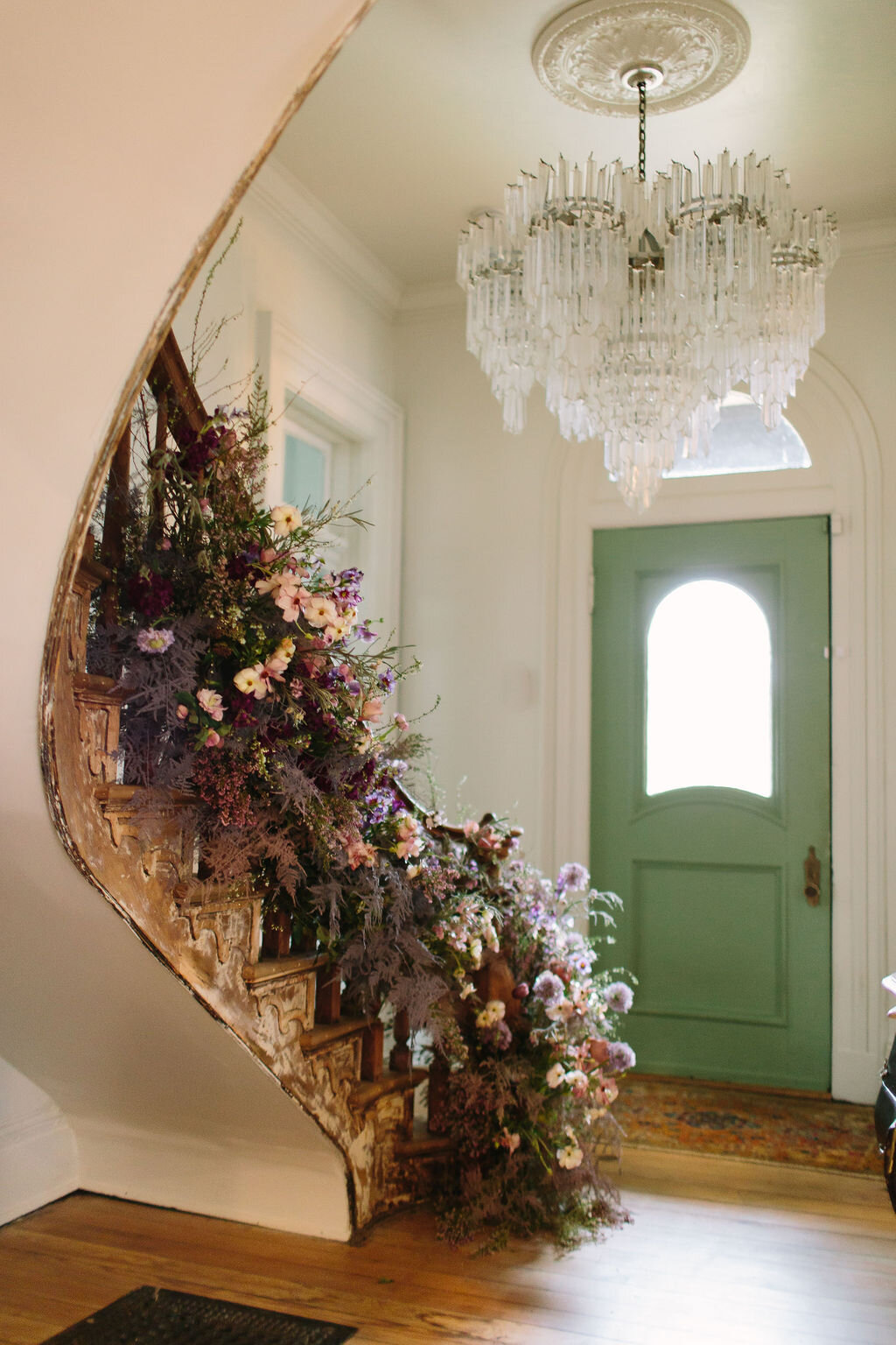 Spiral staircase with a lush, airy floral installation in a lavender and lilac color palette with spirea, painted plumosa ferns, heather, allium, ranunculus, and garden roses. Nashville Wedding Floral Design.