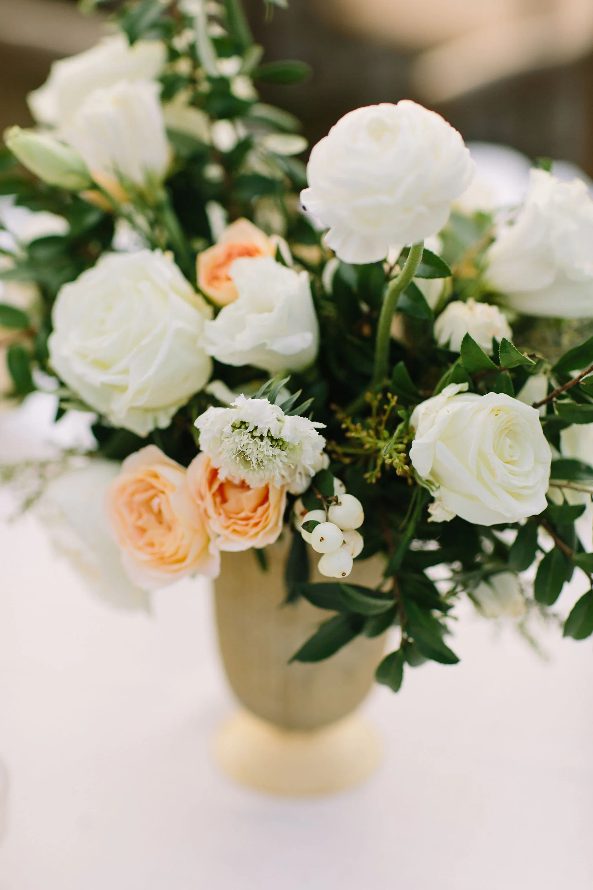 Whimsical floral centerpiece in a gold compote vase with white ranunculus, garden roses, and greenery. Nashville wedding florist at Bloomsbury Farm.