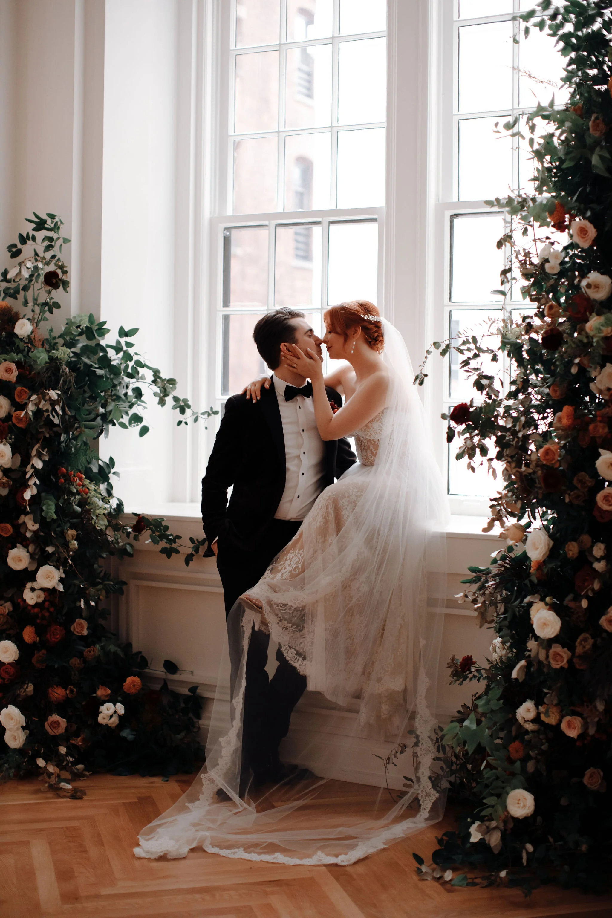 Growing floral installation on either side of the window for the wedding ceremony backdrop, with untamed greenery, rusty orange and burnt sienna garden roses, and lots of texture. Nashville wedding florist at the Noelle hotel.