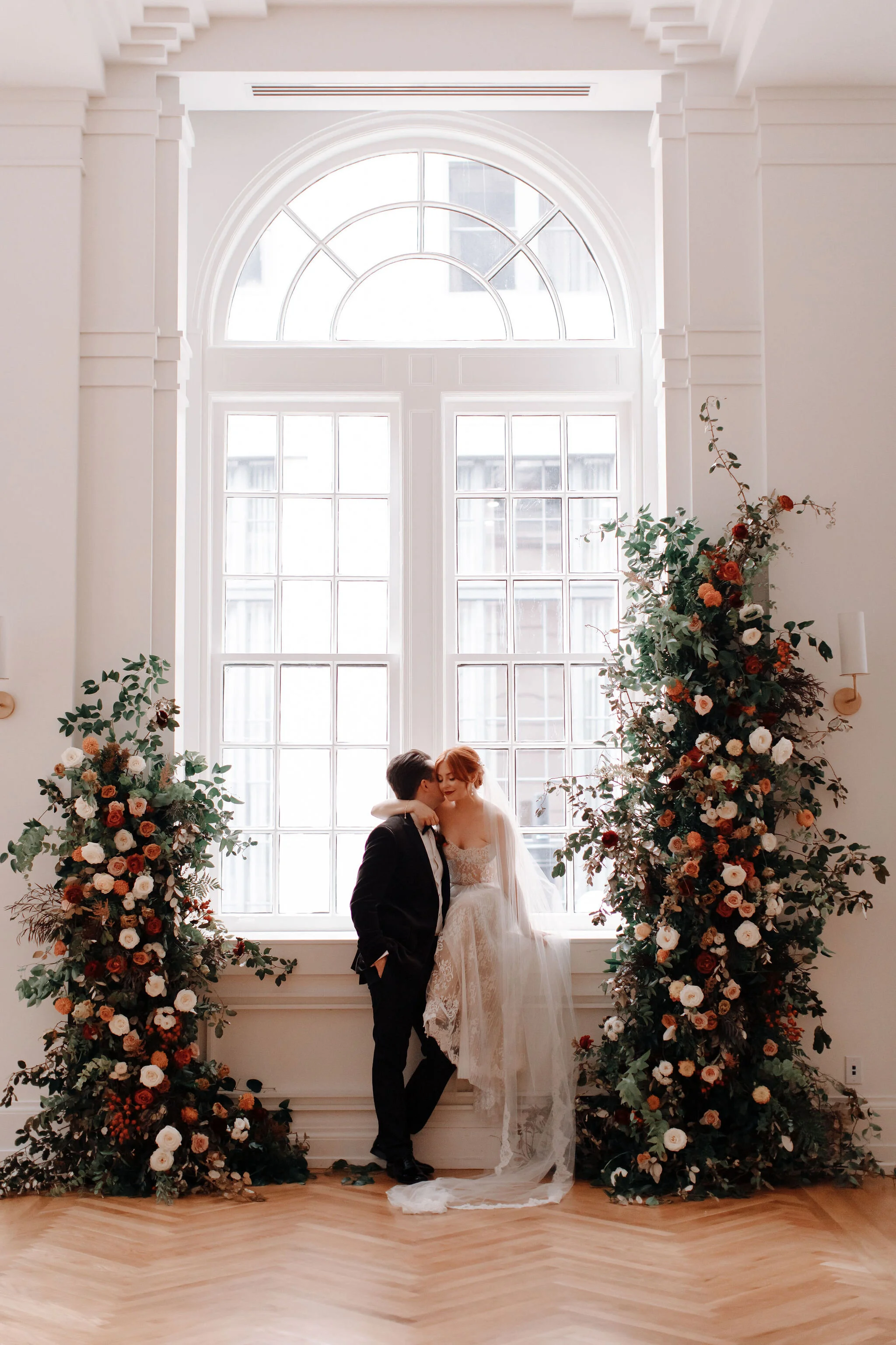 Growing floral installation on either side of the window for the wedding ceremony backdrop, with untamed greenery, rusty orange and burnt sienna garden roses, and lots of texture. Nashville wedding florist at the Noelle hotel.
