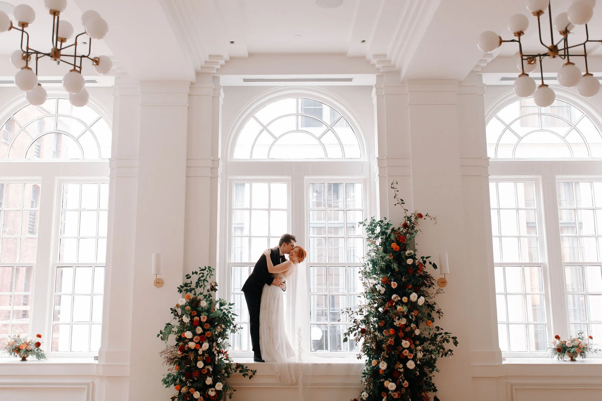 Growing floral installation on either side of the window for the wedding ceremony backdrop, with untamed greenery, rusty orange and burnt sienna garden roses, and lots of texture. Nashville wedding florist at the Noelle hotel.