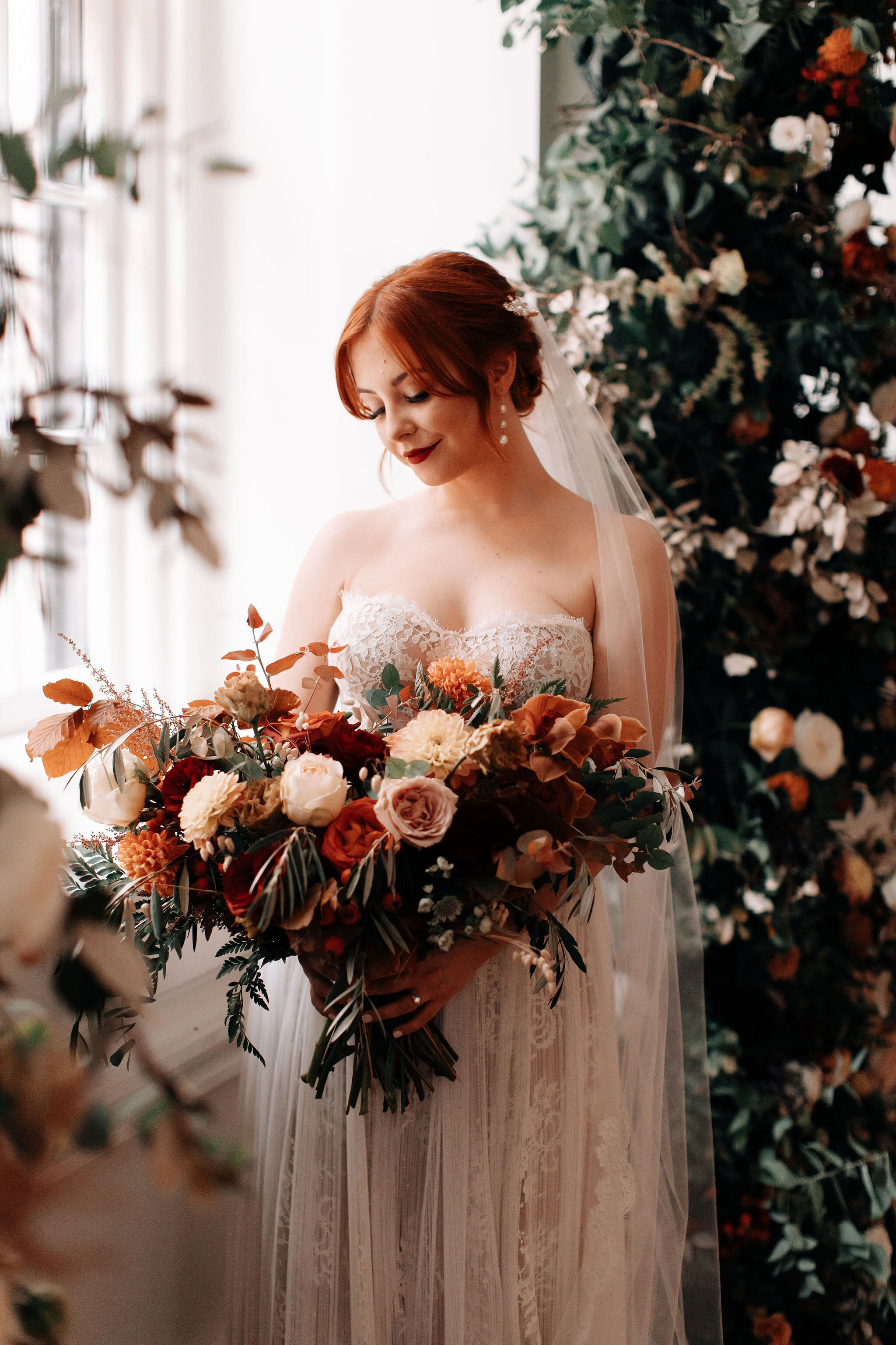 Bridal bouquet in shades of burnt orange, rust, burgundy, copper, and greenery, with dahlias, ranunculus, rosehips, and olive branches. Nashville wedding floral designer.
