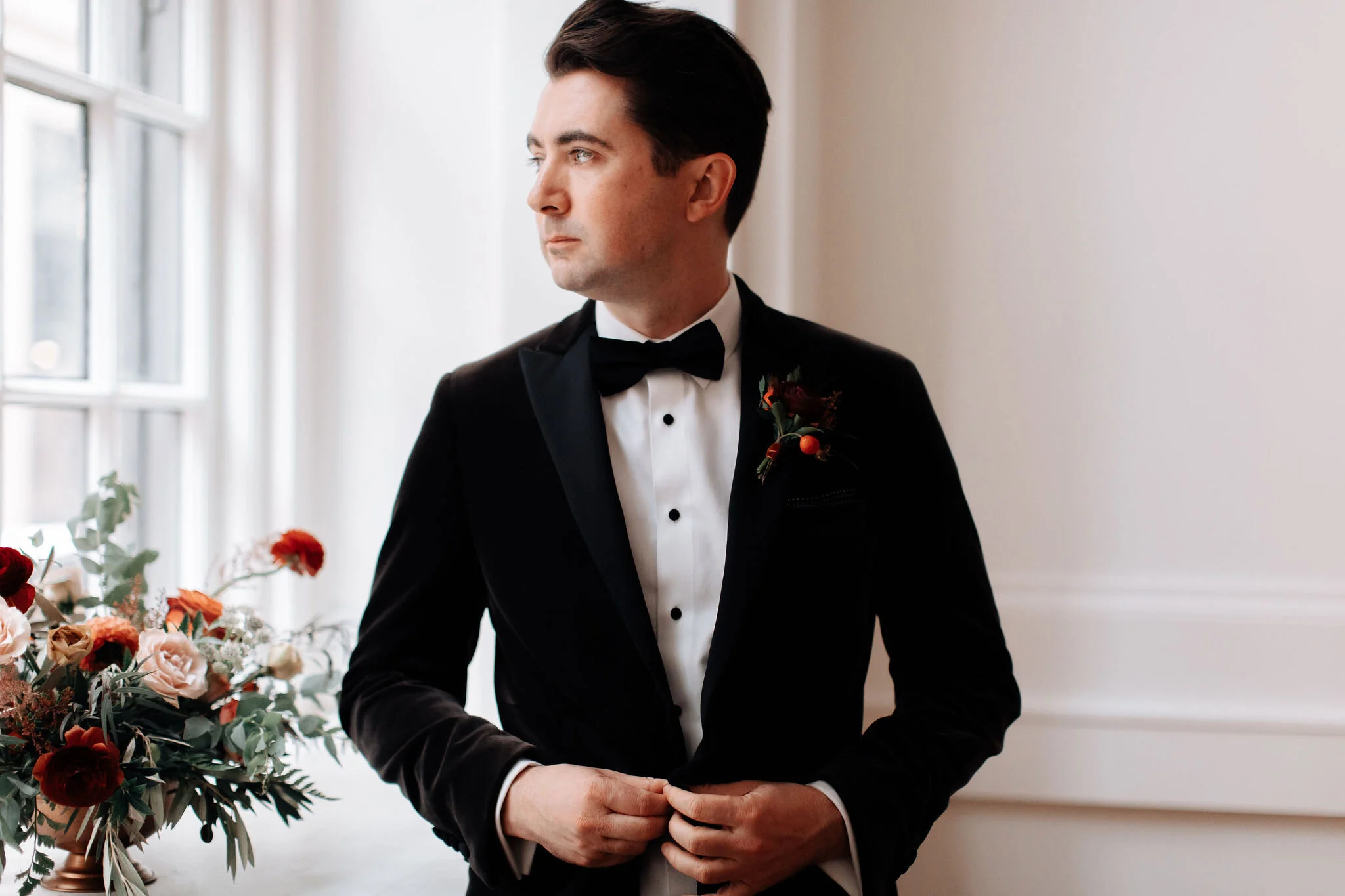 Fall groom boutonniere with burgundy ranunculus, rosehips, texture, and olive branches. Nashville wedding floral design.