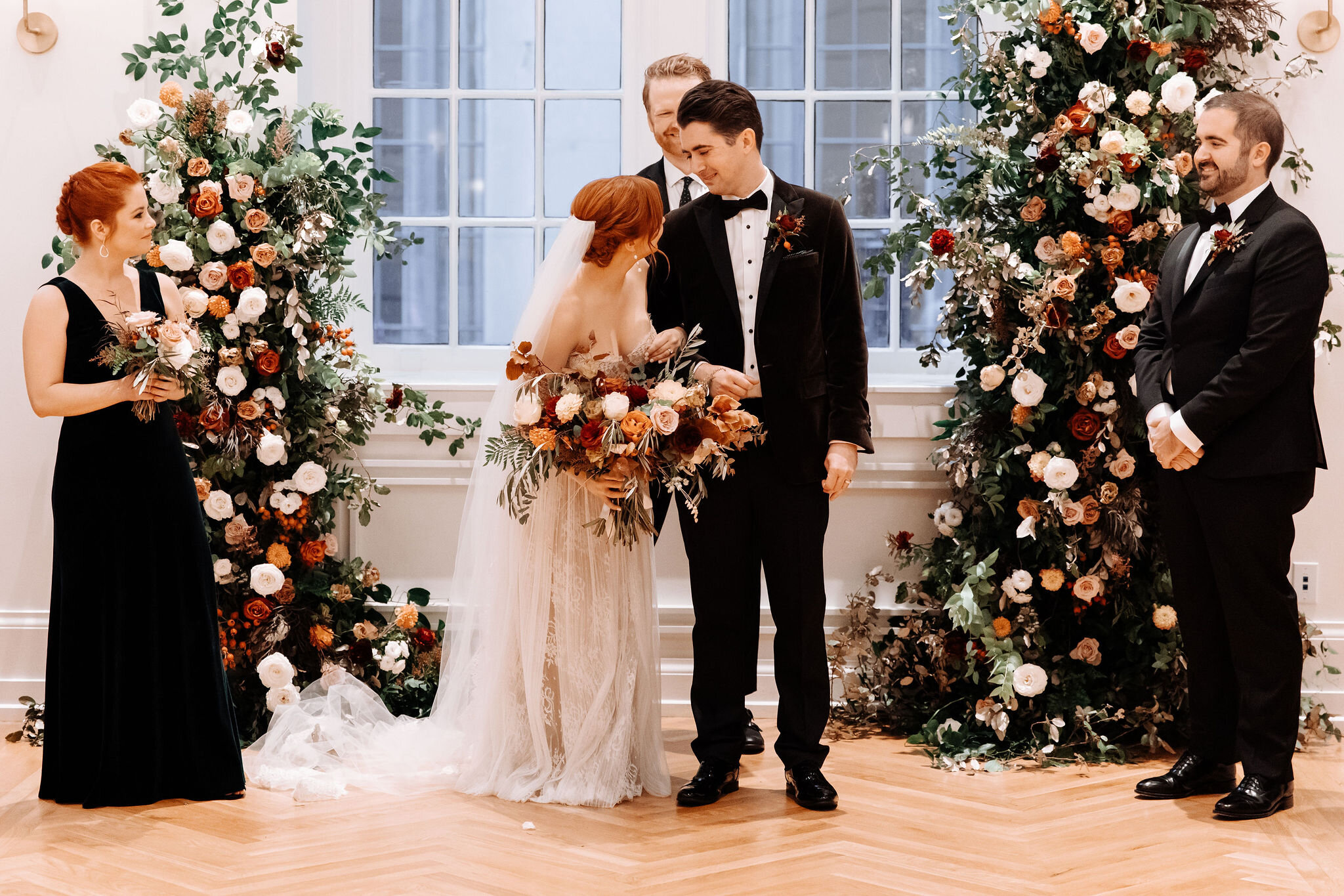 Growing floral installation on either side of the window for the wedding ceremony backdrop, with untamed greenery, rusty orange and burnt sienna garden roses, and lots of texture. Nashville wedding florist at the Noelle hotel.
