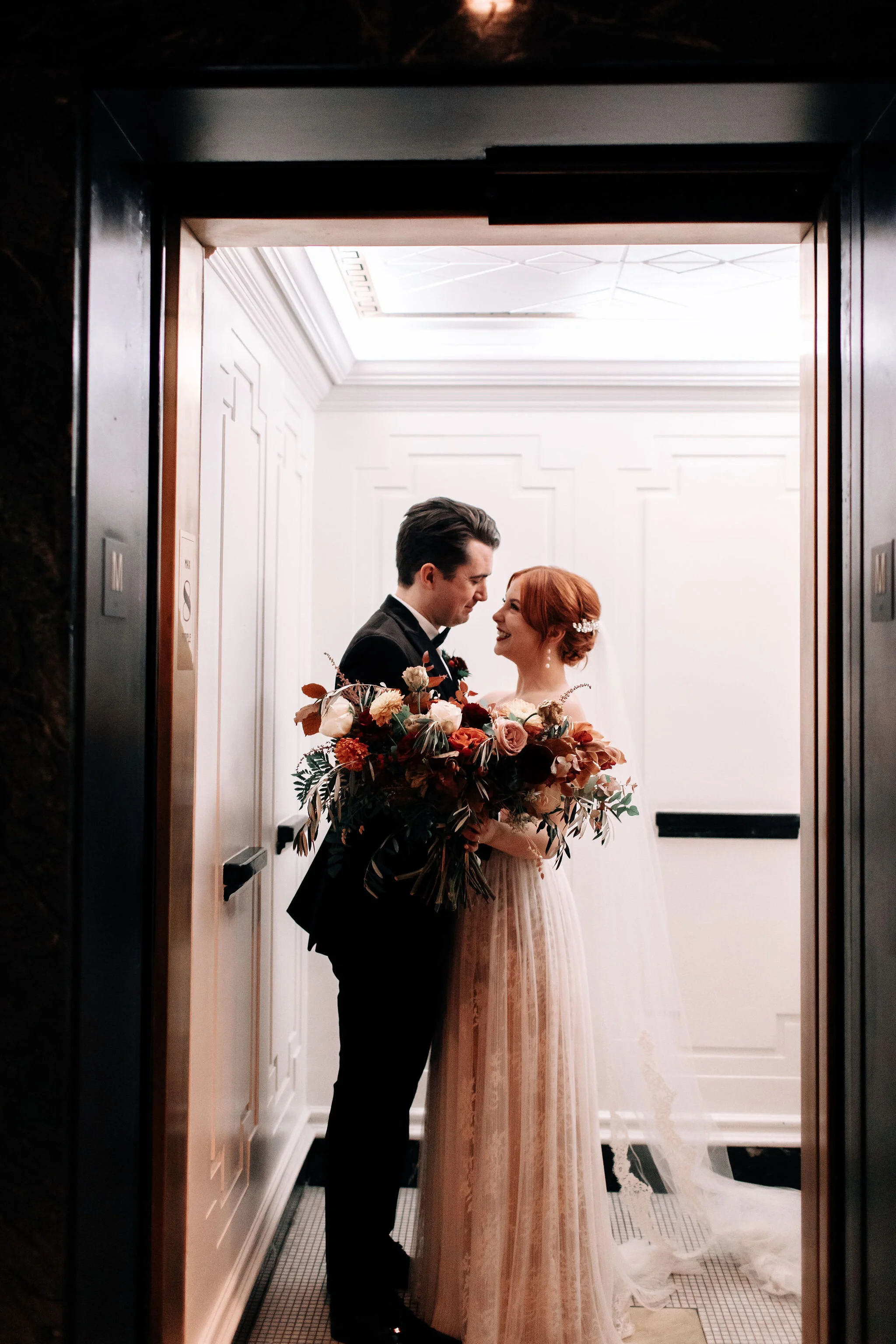 Bridal bouquet in shades of burnt orange, rust, burgundy, copper, and greenery, with dahlias, ranunculus, rosehips, and olive branches. Nashville wedding floral designer.