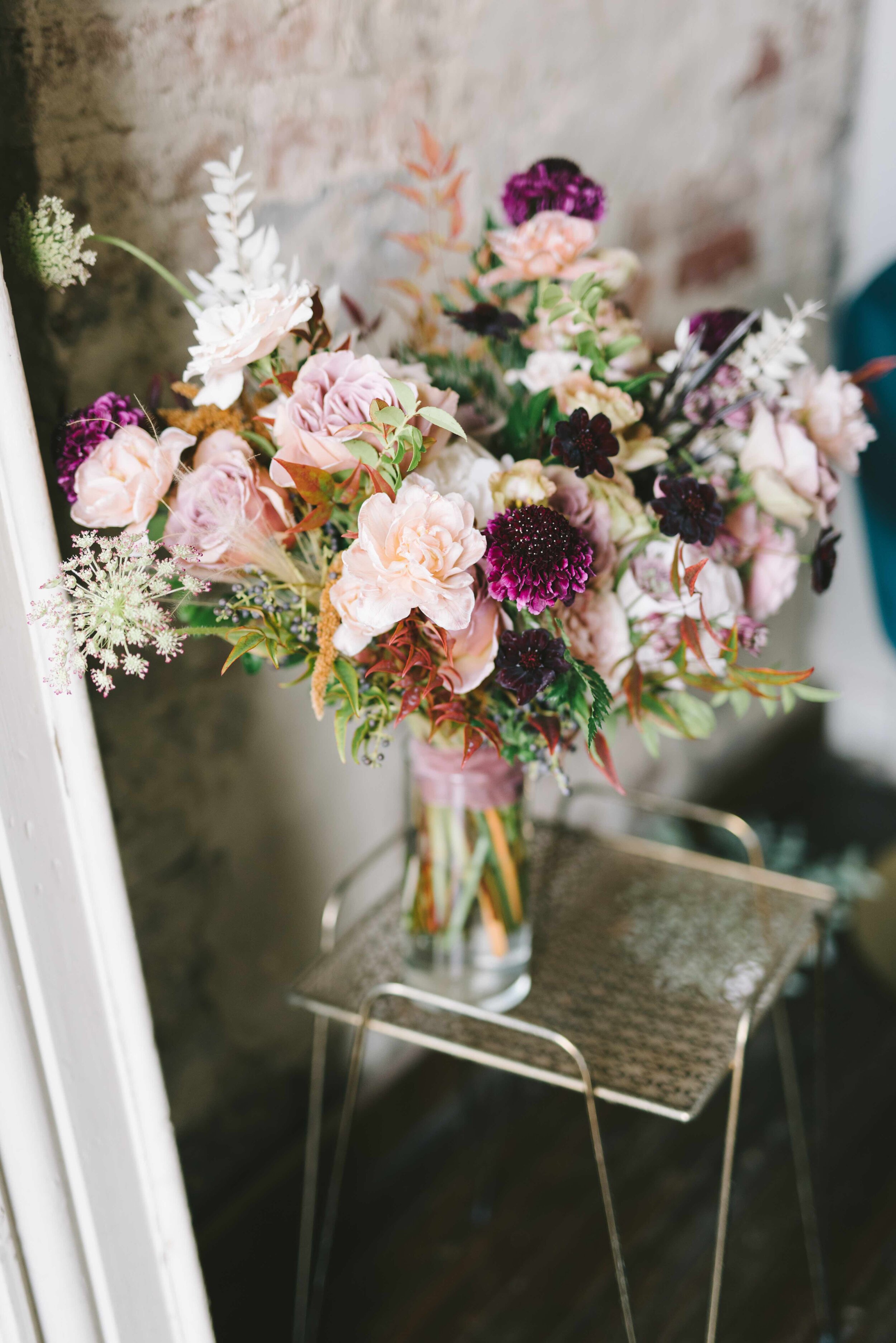 Whimsical bridal bouquet with mauve and blush garden roses and ranunculus, chocolate cosmos, chocolate lace flower, privet berries, white ferns, eggplant scabiosa, and natural greenery. Nashville wedding florist at the Cordelle.