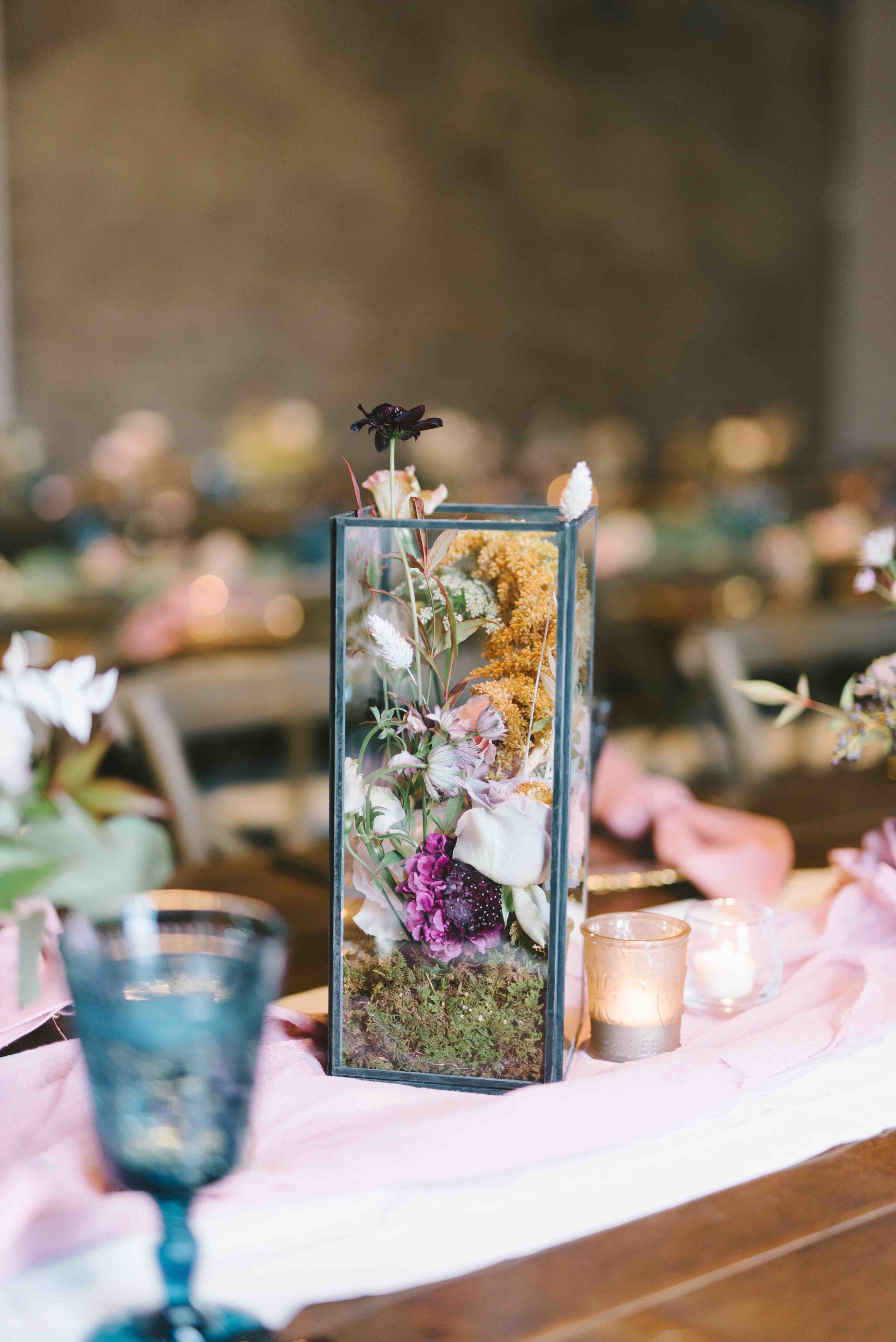 \Whimsical floral terrarium centerpieces with moss, dried white ferns, eggplant scabiosa, chocolate cosmos, privet berries, champagne, mauve, and blush roses, white tulips. and fall foliage and greenery. Nashville wedding florist at the Cordelle.