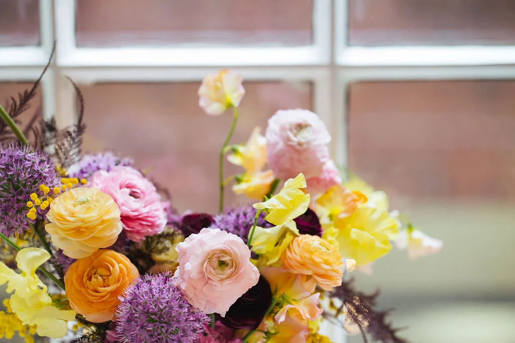 Modern, colorful bridal bouquet with yellow sweet peas, purple allium, pink and peach ranunculus, and painted eggplant plums fern. Nashville wedding florist.