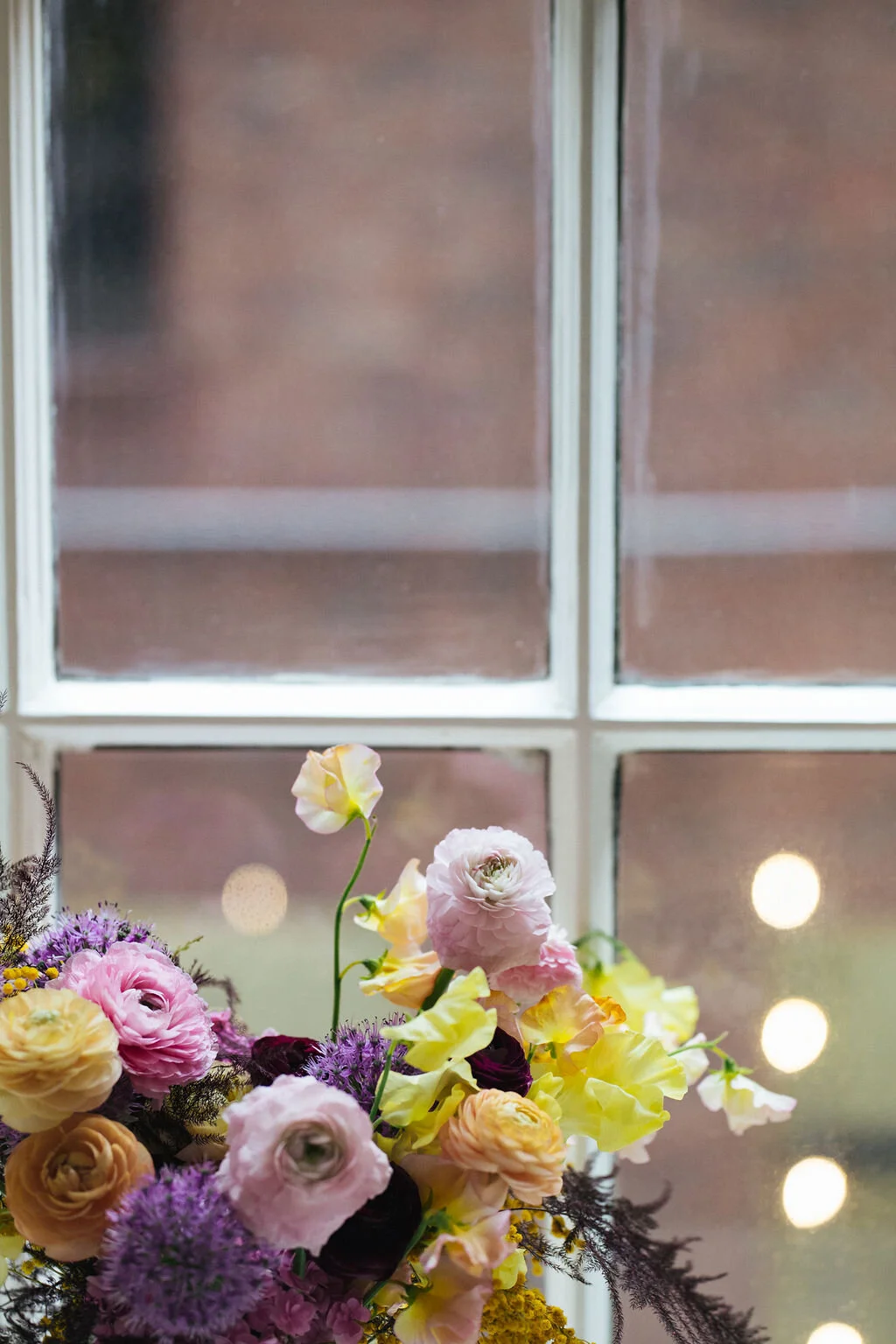 Modern, colorful bridal bouquet with yellow sweet peas, purple allium, pink and peach ranunculus, golden acacia, and painted eggplant plums fern. Nashville wedding florist.
