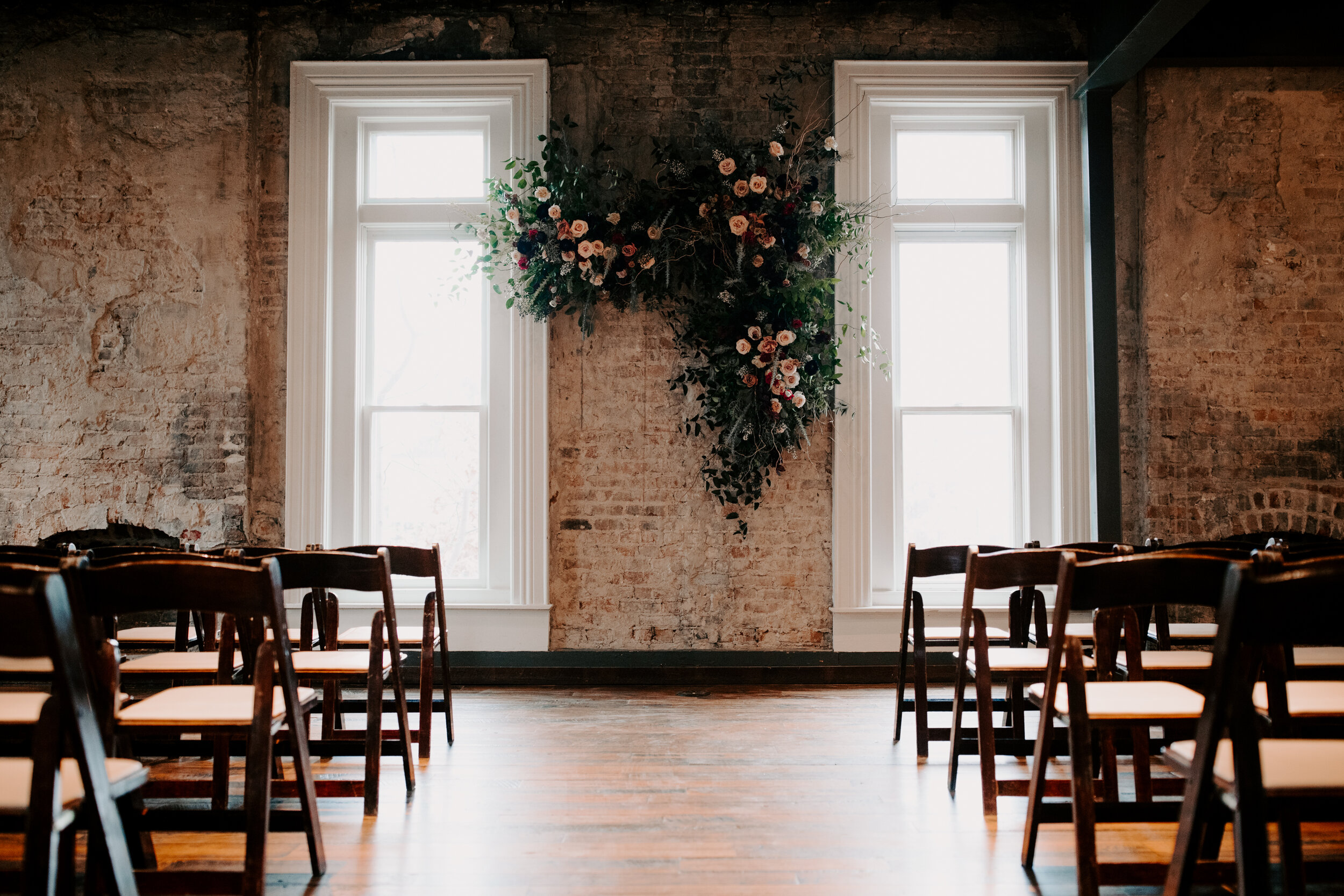 Organic, hanging floral installation for the wedding ceremony backdrop with lush greenery, curly willow branches, and earth toned and burgundy flowers. Nashville wedding florist at the Cordelle.