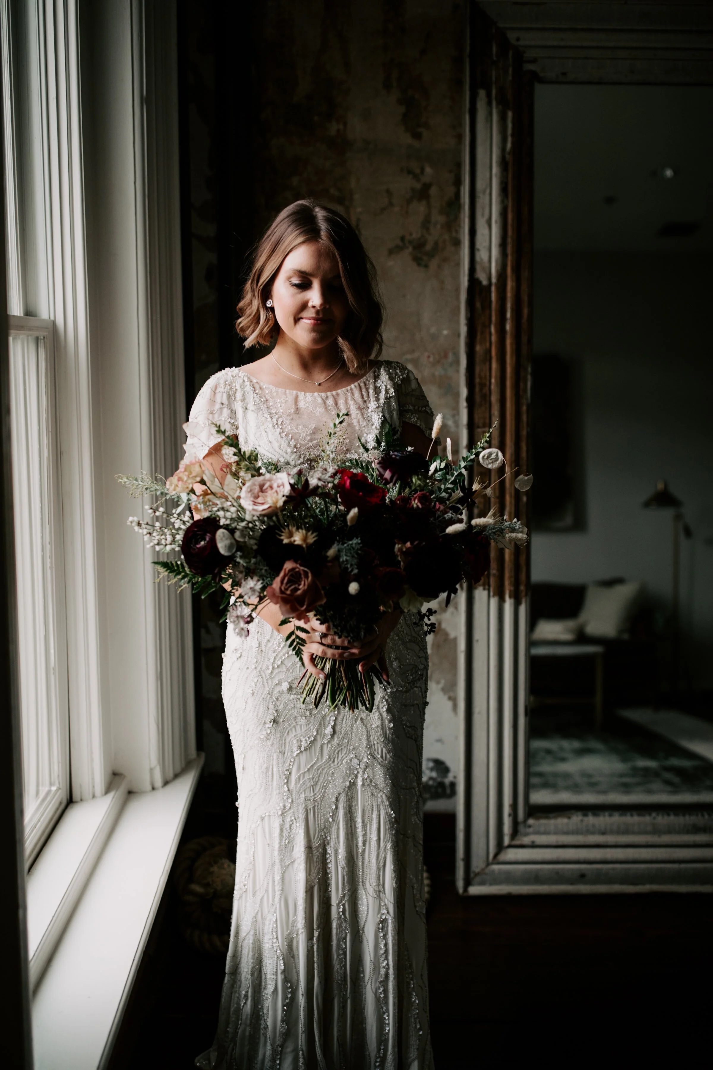Loose, whimsical winter bridal bouquet with eggplant, blush, mauve, and burgundy garden roses and ranunculus, dried flowers, and natural, untamed greenery. Nashville wedding floral design at the Cordelle.