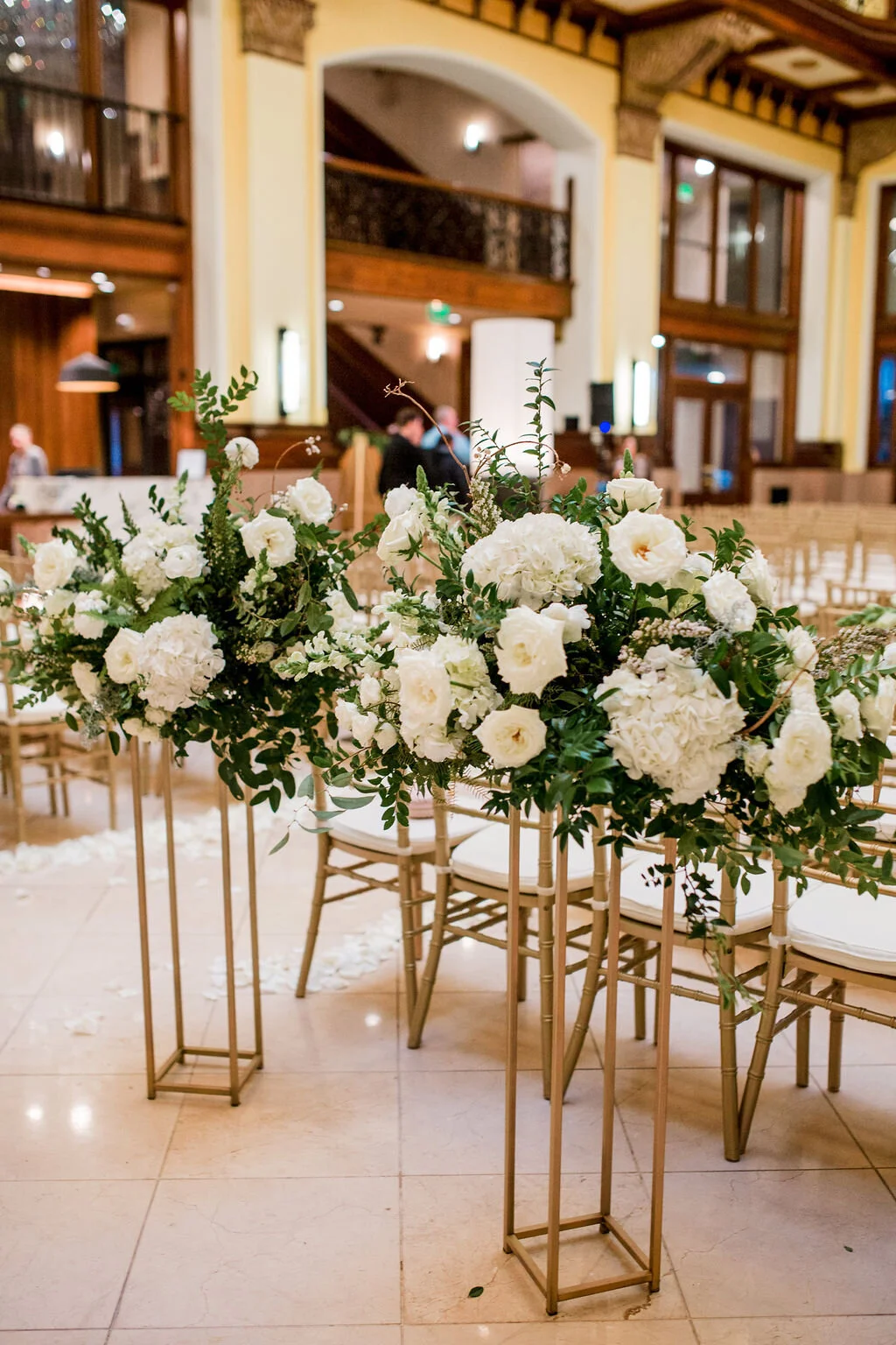 Elevated gold stands with lush floral centerpieces of white garden roses, ranunculus, snapdragons, and natural, untamed greenery. Nashville wedding florist at Union Station.