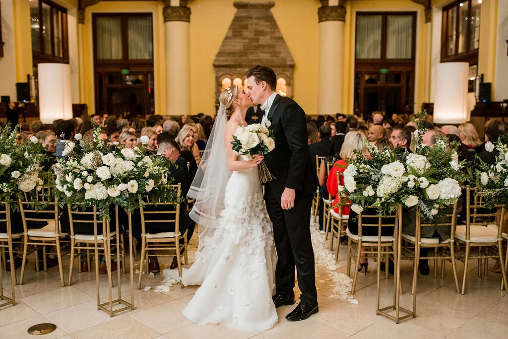 Elevated gold stands with lush floral centerpieces of white garden roses, ranunculus, snapdragons, and natural, untamed greenery. Nashville wedding florist at Union Station.