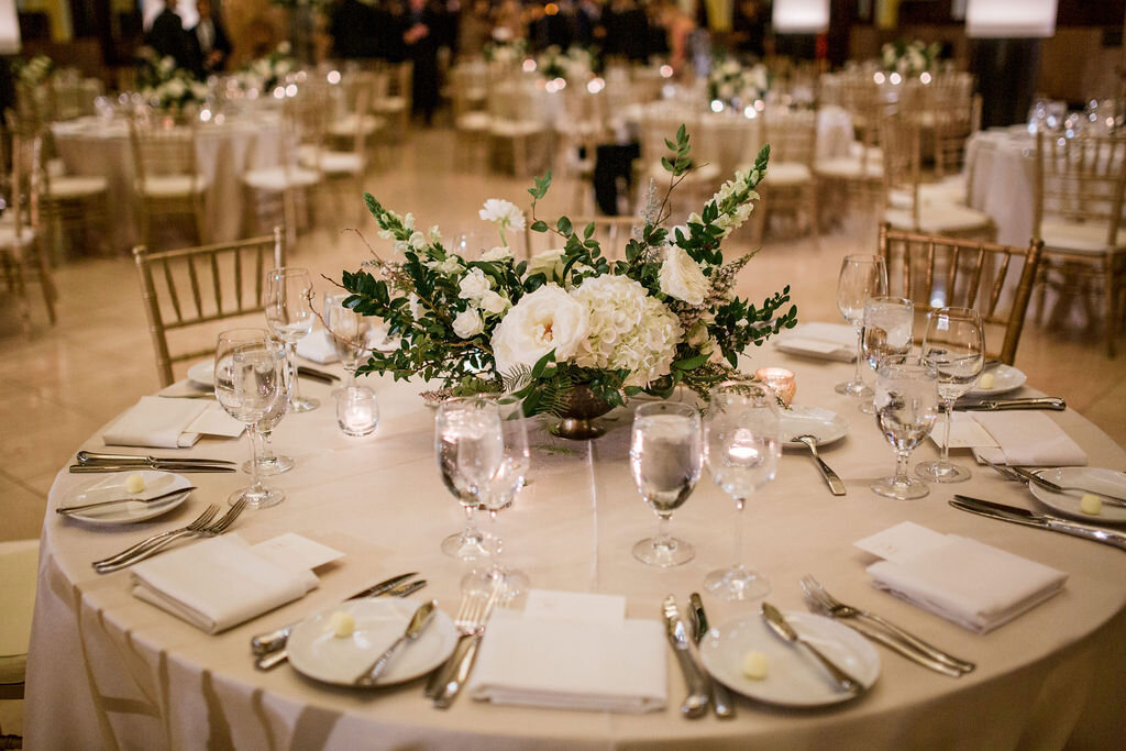 Low floral centerpiece in a gold compote overflowing with white garden roses, hydrangeas, lisianthus, snapdragons, ranunculus, and natural dark greenery. Elegant winter wedding floral design at Union Station, Nashville.