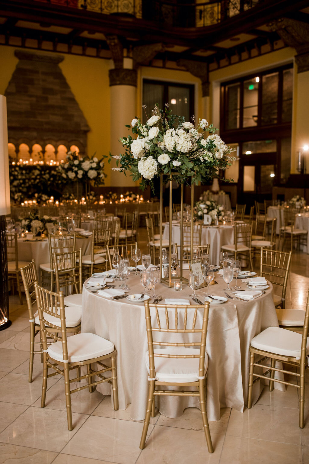Elevated gold stands with lush floral centerpieces of white garden roses, ranunculus, snapdragons, and natural, untamed greenery. Nashville wedding florist at Union Station.