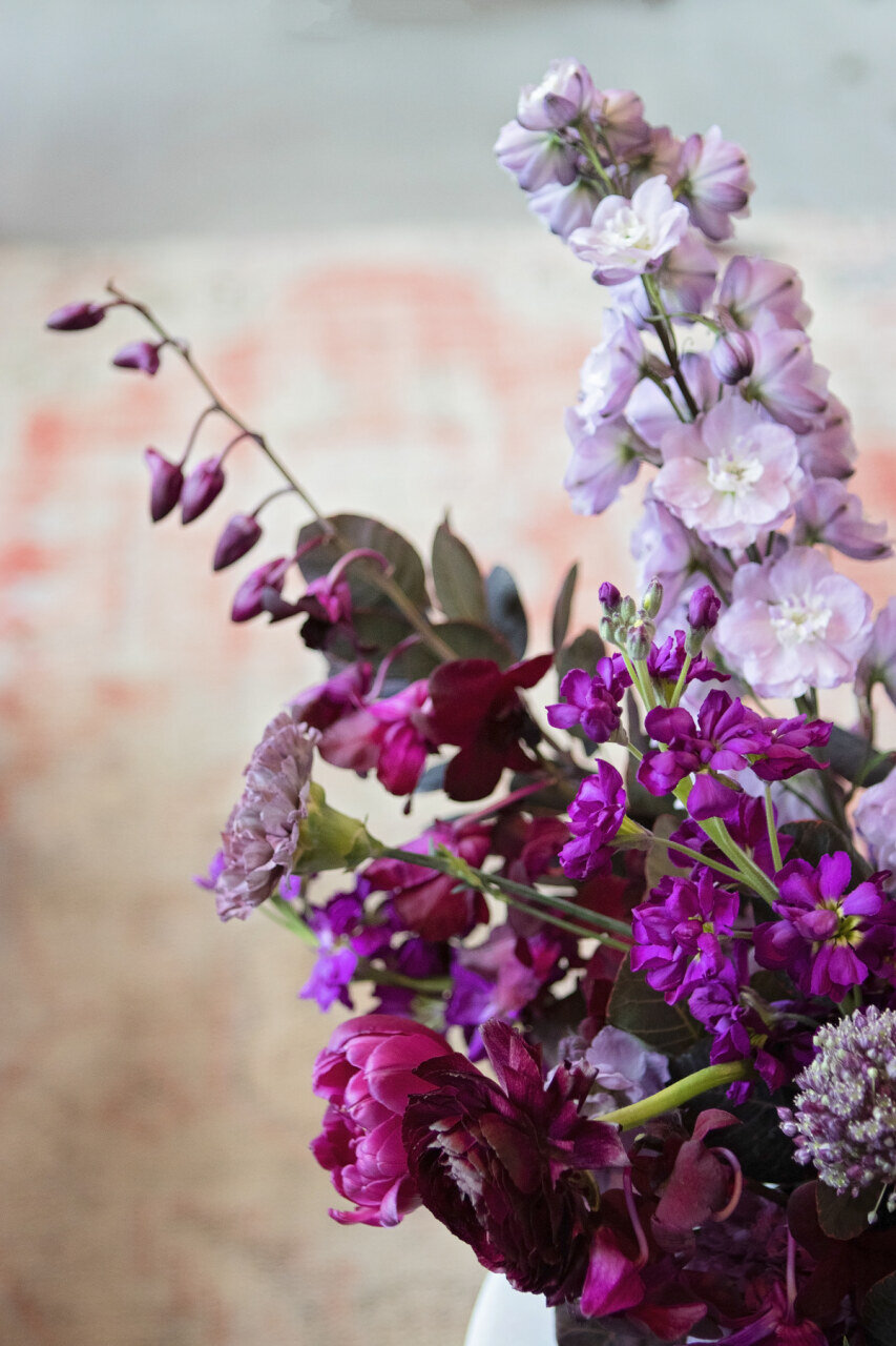 Low, organic floral arrangement in an eggplant, lavender, and deep purple color palette with delphinium, orchids, smokebush, tulips, allium, ranunculus, antique carnations, and garden roses. Nashville wedding florist, Rosemary & Finch.