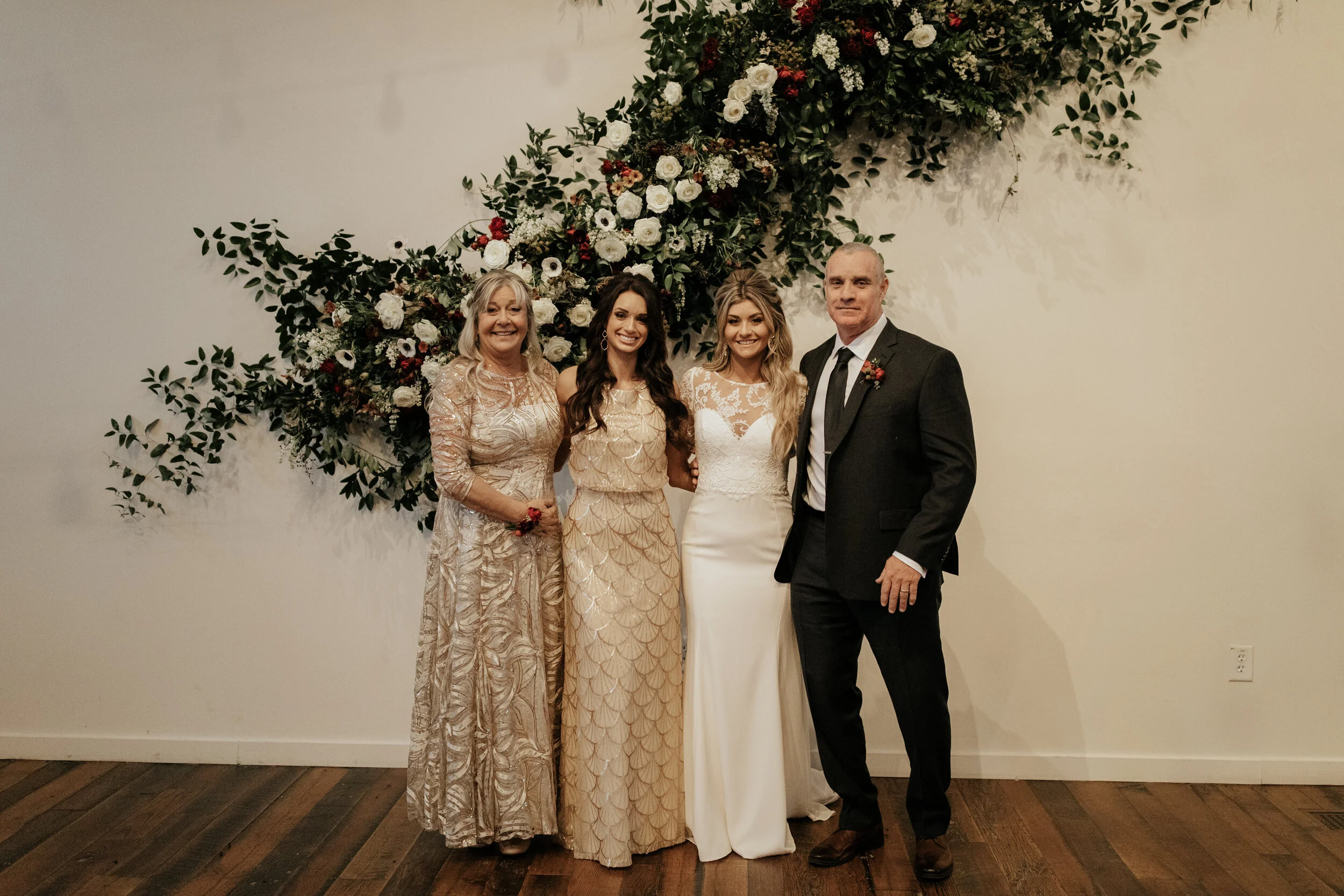 Asymmetrical floral installation growing up the white wall of the Cordelle with natural, untamed greenery, burgundy and white garden roses and ranunculus, and organic textures. Nashville wedding florist.