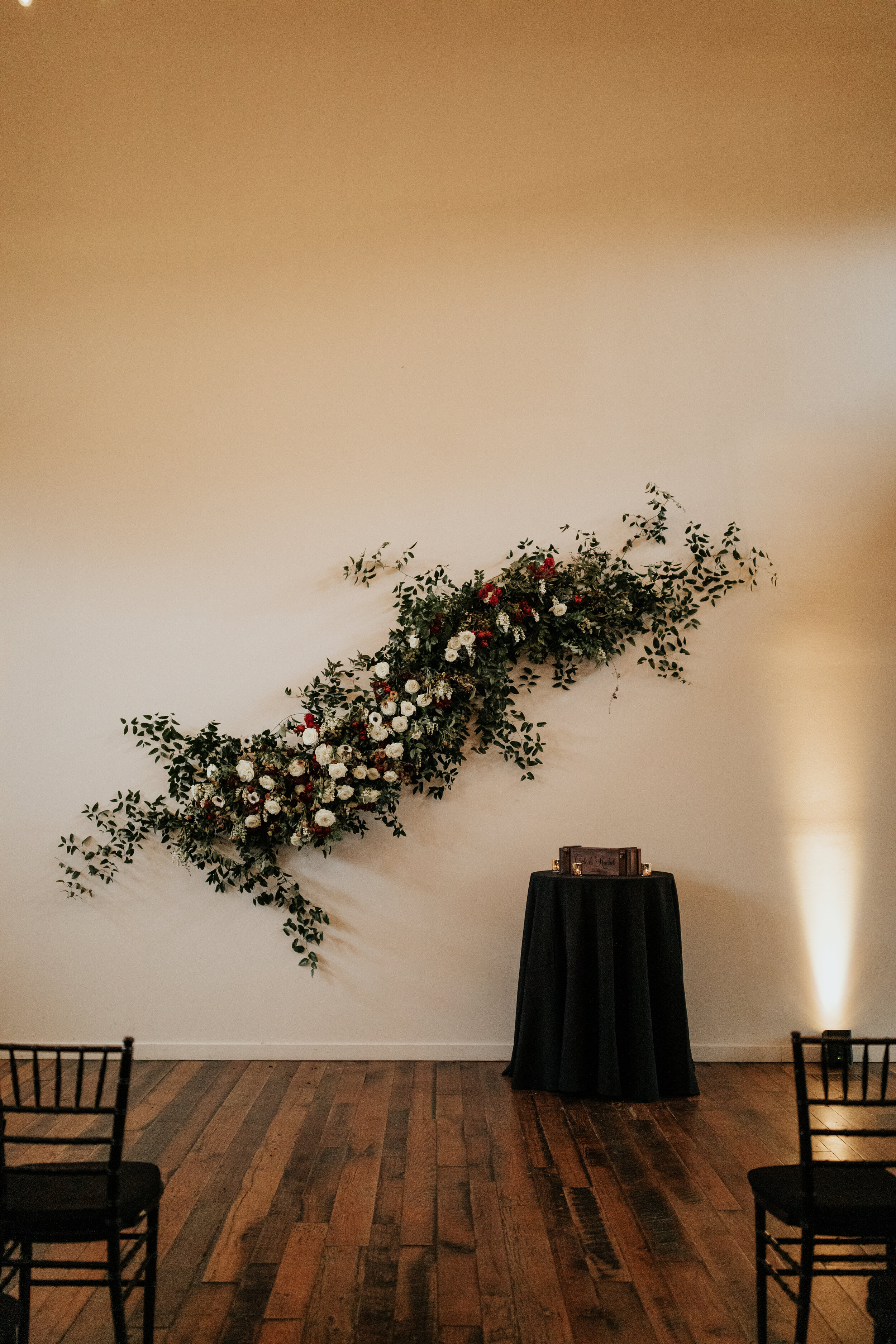 Asymmetrical floral installation growing up the white wall of the Cordelle with natural, untamed greenery, burgundy and white garden roses and ranunculus, and organic textures. Nashville wedding florist.
