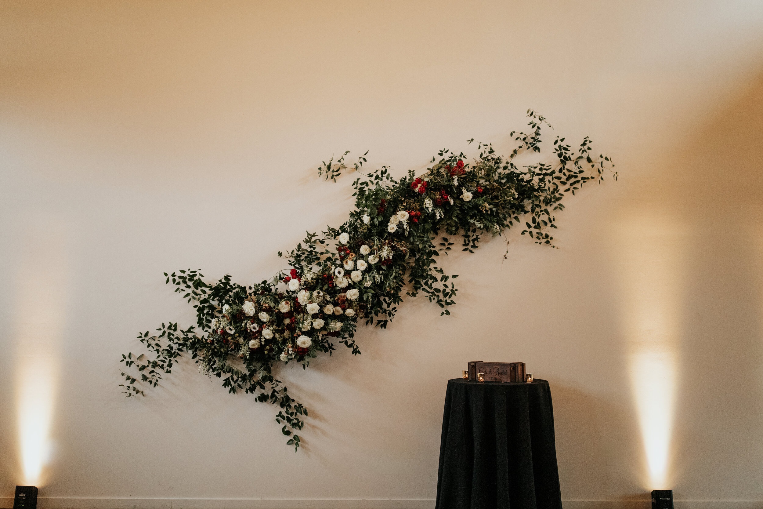 Asymmetrical floral installation growing up the white wall of the Cordelle with natural, untamed greenery, burgundy and white garden roses and ranunculus, and organic textures. Nashville wedding florist.
