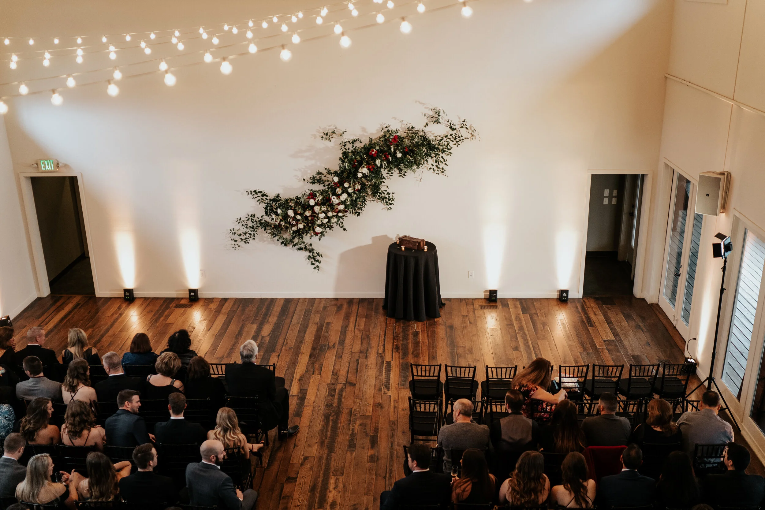 Asymmetrical floral installation growing up the white wall of the Cordelle with natural, untamed greenery, burgundy and white garden roses and ranunculus, and organic textures. Nashville wedding florist.