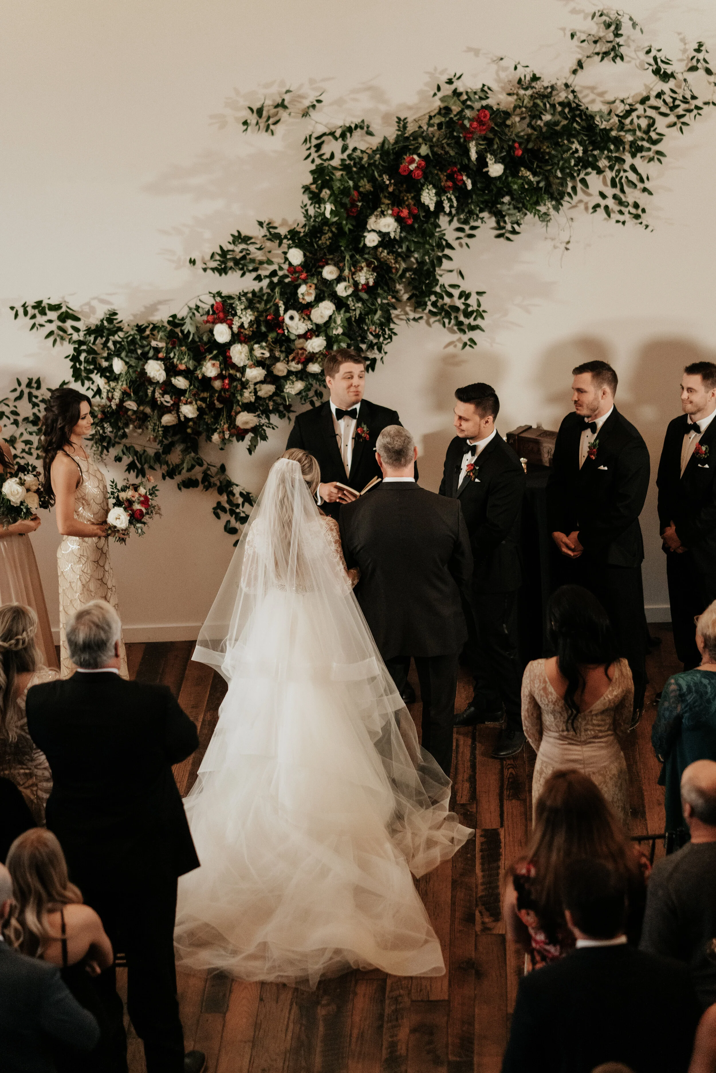 Asymmetrical floral installation growing up the white wall of the Cordelle with natural, untamed greenery, burgundy and white garden roses and ranunculus, and organic textures. Nashville wedding florist.
