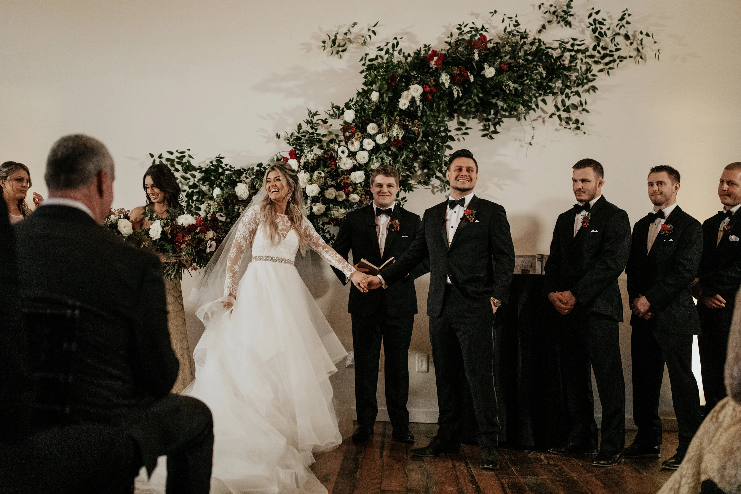 Asymmetrical floral installation growing up the white wall of the Cordelle with natural, untamed greenery, burgundy and white garden roses and ranunculus, and organic textures. Nashville wedding florist.