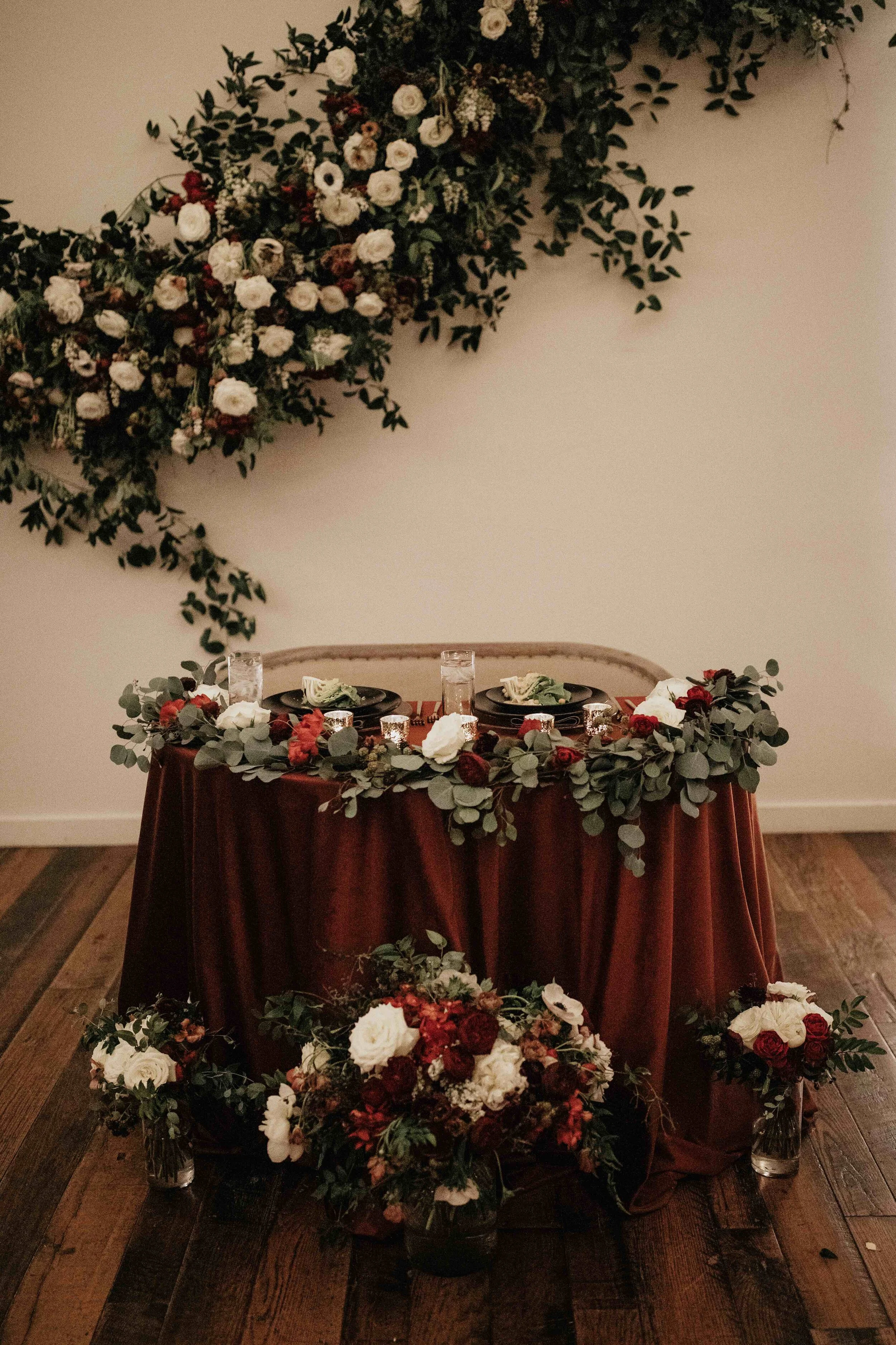 Asymmetrical floral installation growing up the white wall of the Cordelle with natural, untamed greenery, burgundy and white garden roses and ranunculus, and organic textures. Nashville wedding florist.