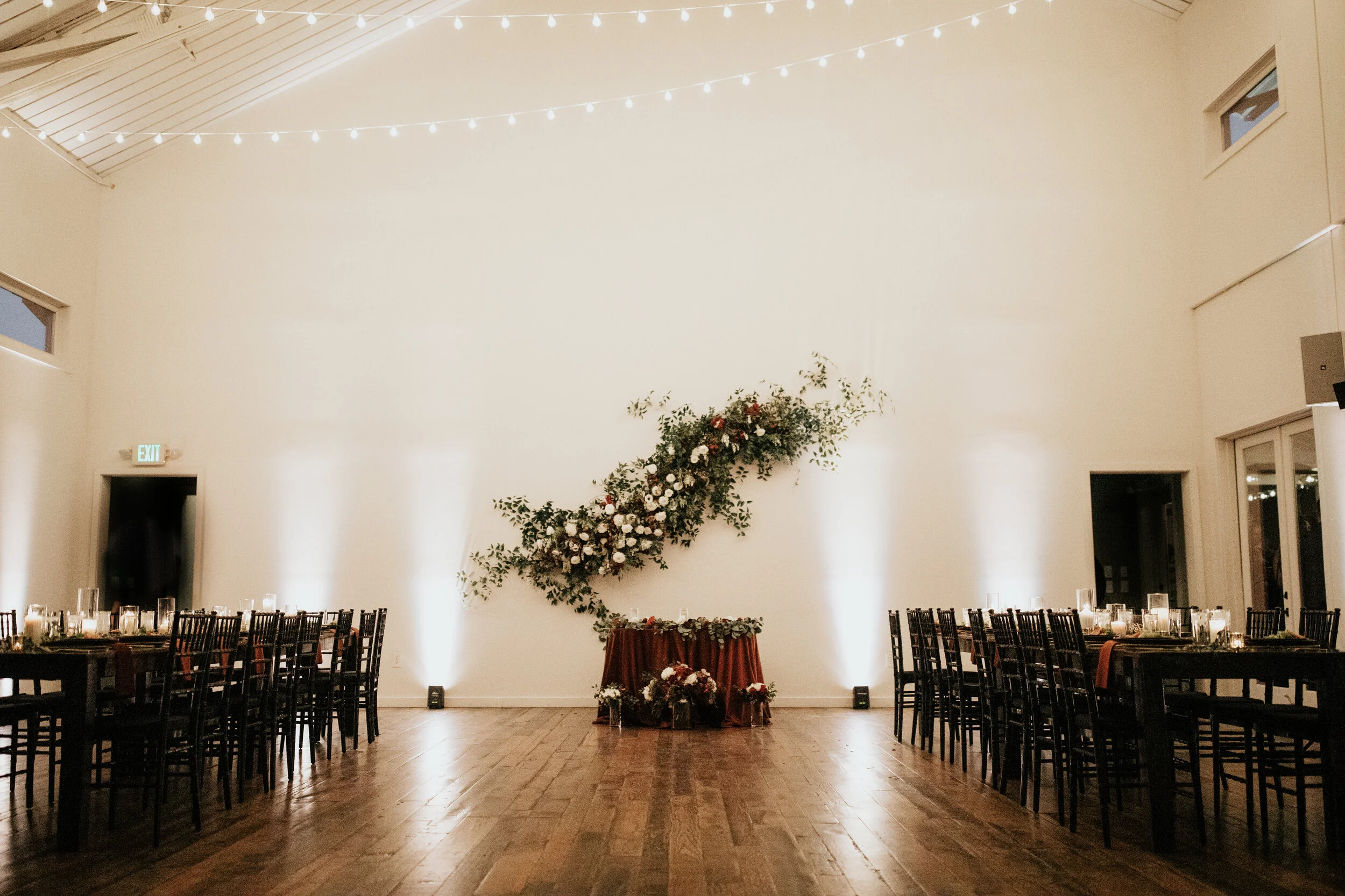 Asymmetrical floral installation growing up the white wall of the Cordelle with natural, untamed greenery, burgundy and white garden roses and ranunculus, and organic textures. Nashville wedding florist.