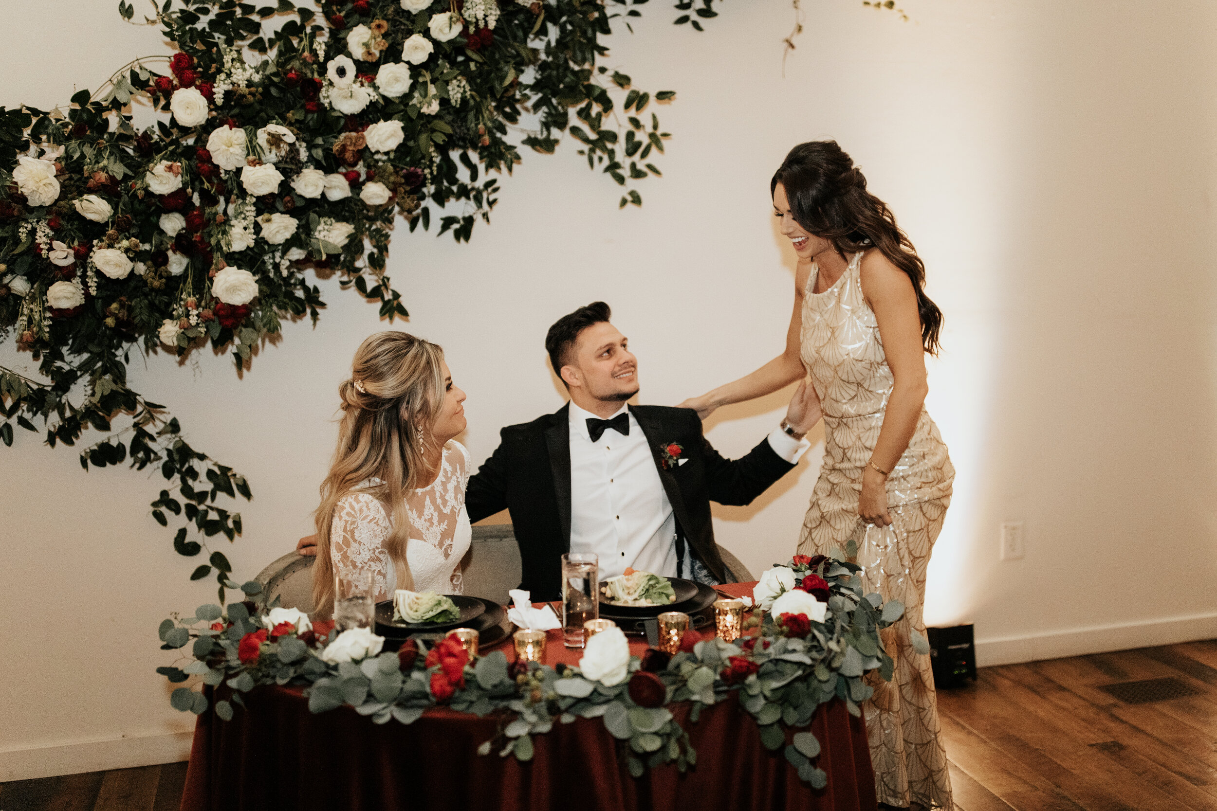Asymmetrical floral installation growing up the white wall of the Cordelle with natural, untamed greenery, burgundy and white garden roses and ranunculus, and organic textures. Nashville wedding florist.