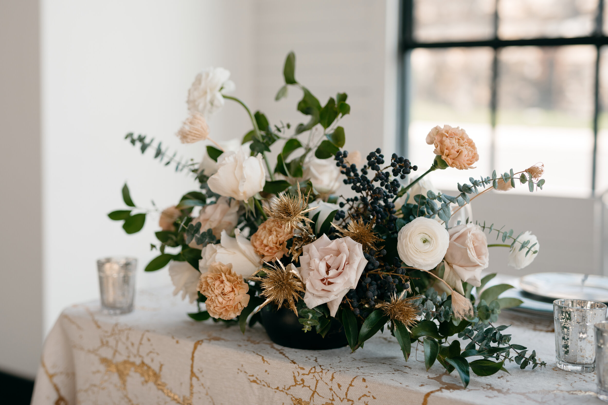 Winter inspiration centerpiece featuring white roses, touches of gold, baby eucalyptus and lush greenery. Nashville wedding florist Rosemary & Finch at OZARI.