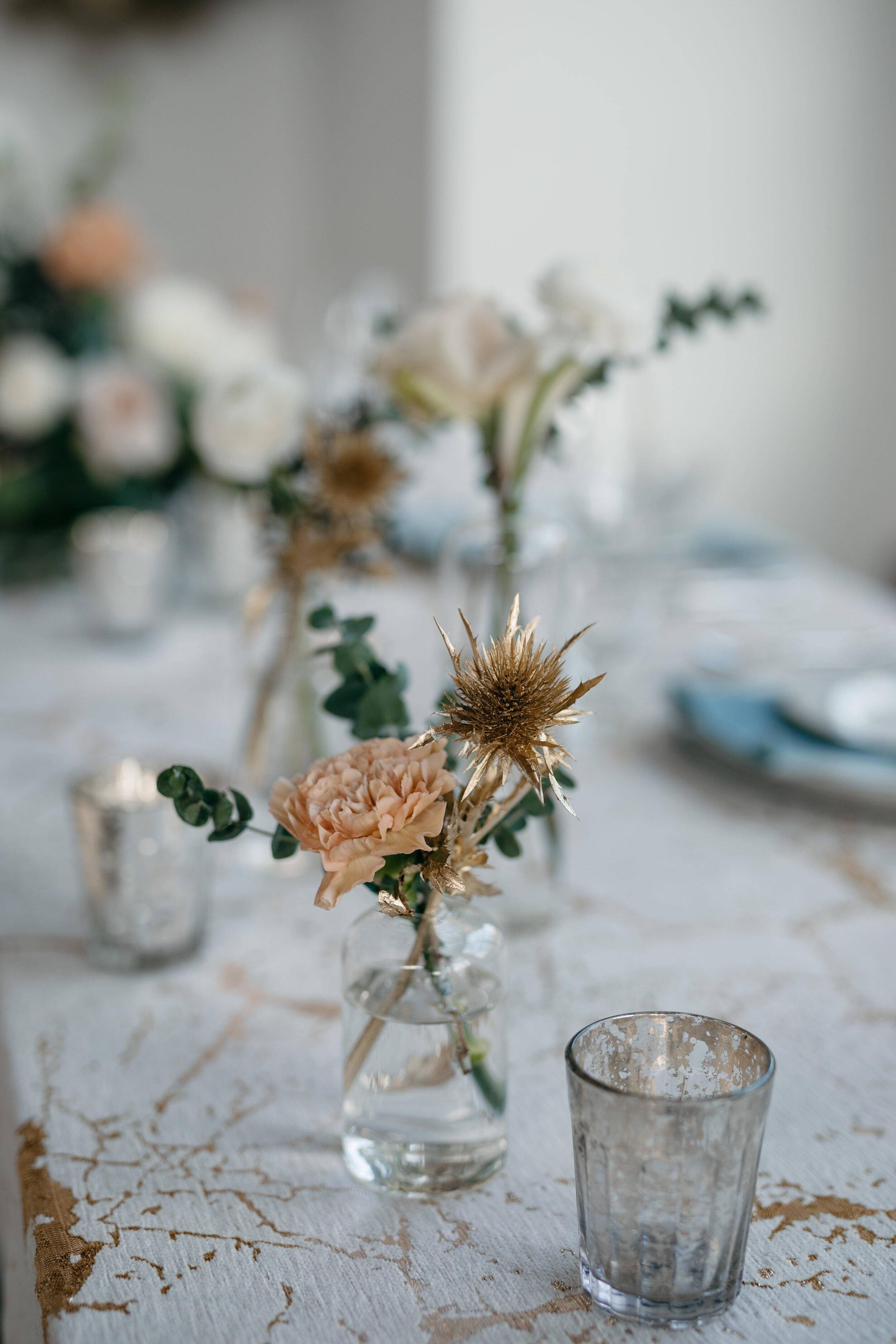 Winter inspiration tablescape featuring sweet bud vases of white roses, touches of gold, baby eucalyptus, and earth tone carnations. Nashville wedding florist Rosemary & Finch at OZARI.