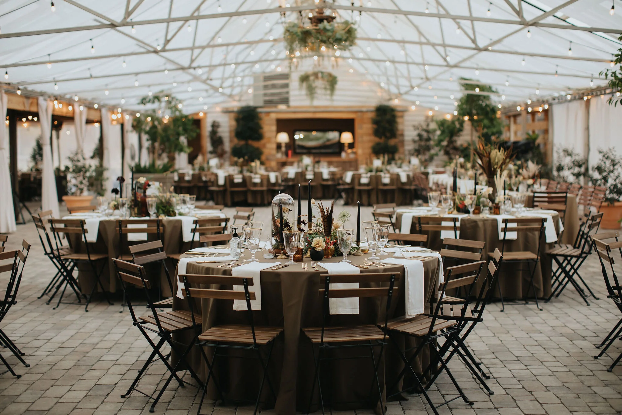 Earthy and romantic – this eclectic tablescape is crafted from pheasant feathers, brass candlesticks, and layered florals. Botanical cloches are filled with fern, moss, chocolate cosmos, and ranunculus. Designed by Nashville wedding floral designer,…
