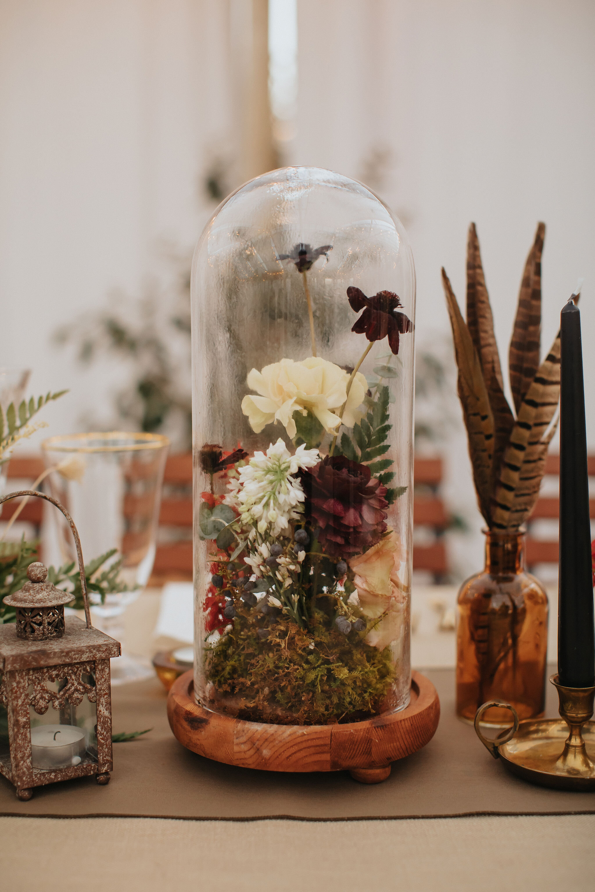Earthy and romantic – this eclectic tablescape is crafted from pheasant feathers, brass candlesticks, and layered florals. Botanical cloches are filled with fern, moss, chocolate cosmos, and ranunculus. Designed by Nashville wedding floral designer,…
