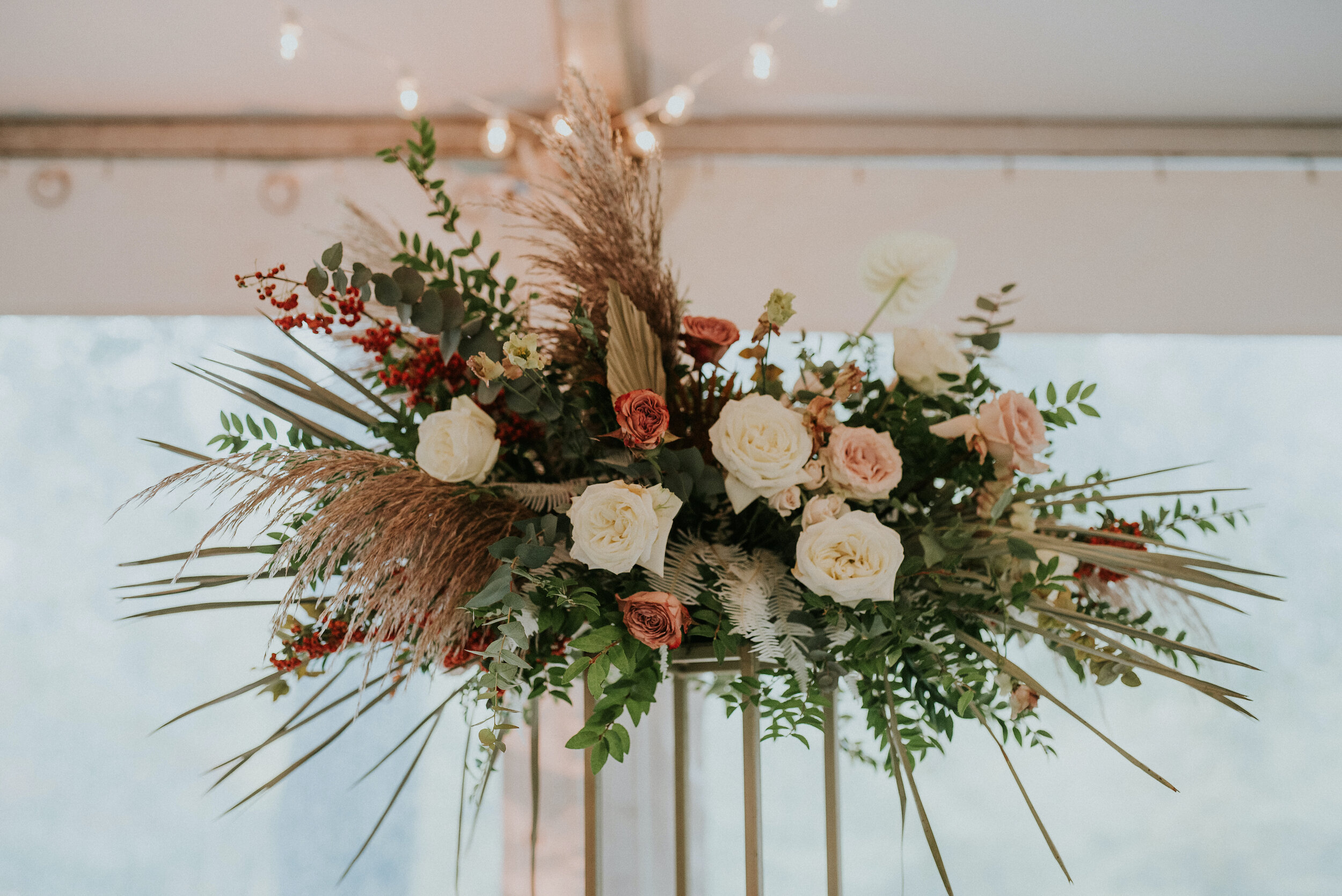 Bohemian and modern yet classically elegant. This wedding perfectly married boho elements of pampas grass, eucalyptus, and dried florals with topical stems of anthurium and orchid. Quicksand roses, cappuccino roses, ilex berry, and rust fern add a p…