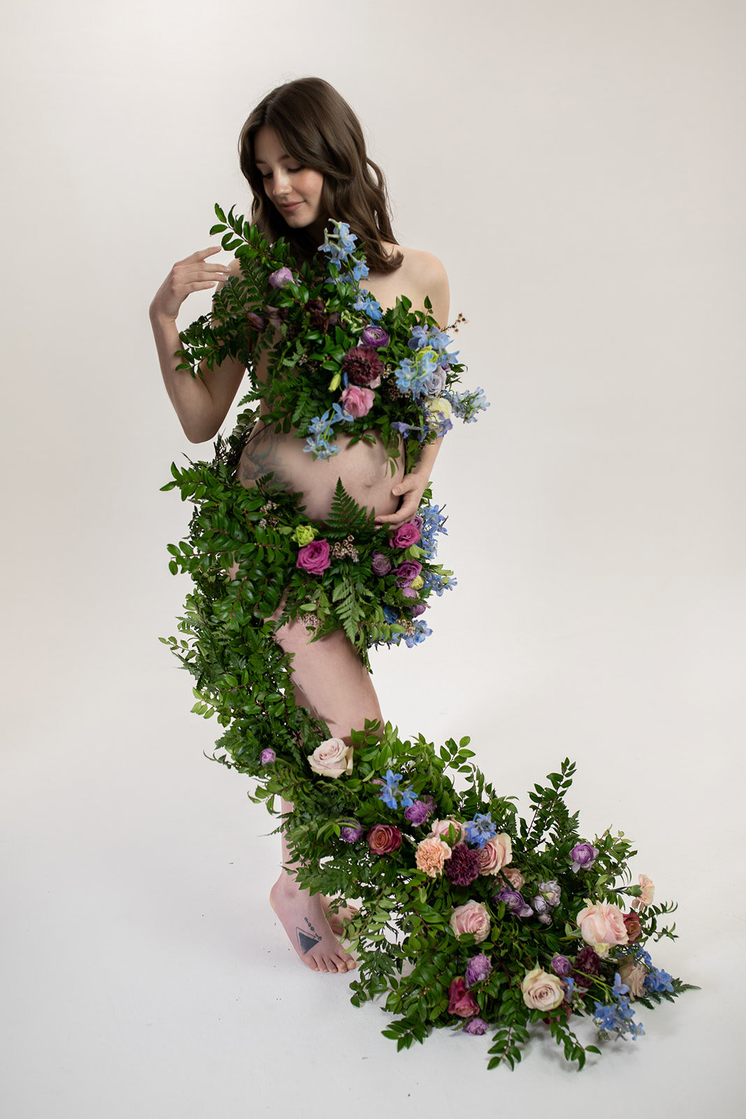 Greek inspired maternity shoot with a wearable floral garland filled with blue delphinium, lavender spray roses, plum ranunculus, blush and fuchsia roses. Designed by wedding florist Rosemary & Finch in Nashville.