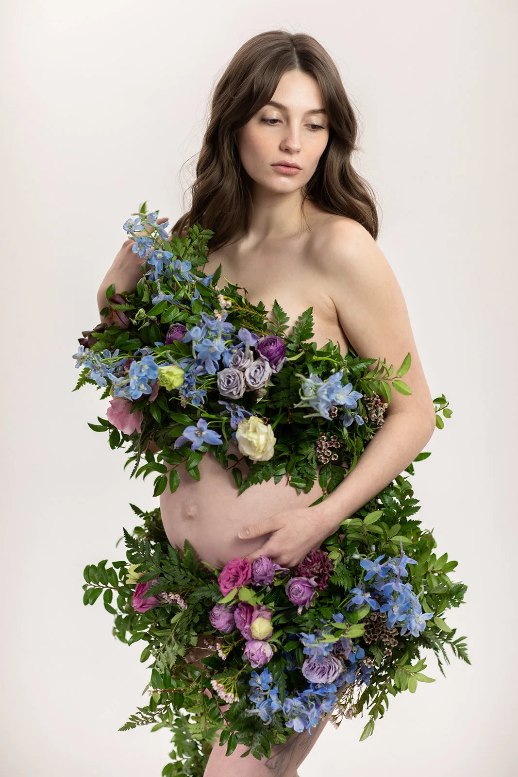 Greek inspired maternity shoot with a wearable floral garland filled with blue delphinium, lavender spray roses, plum ranunculus, blush and fuchsia roses. Designed by wedding florist Rosemary & Finch in Nashville.