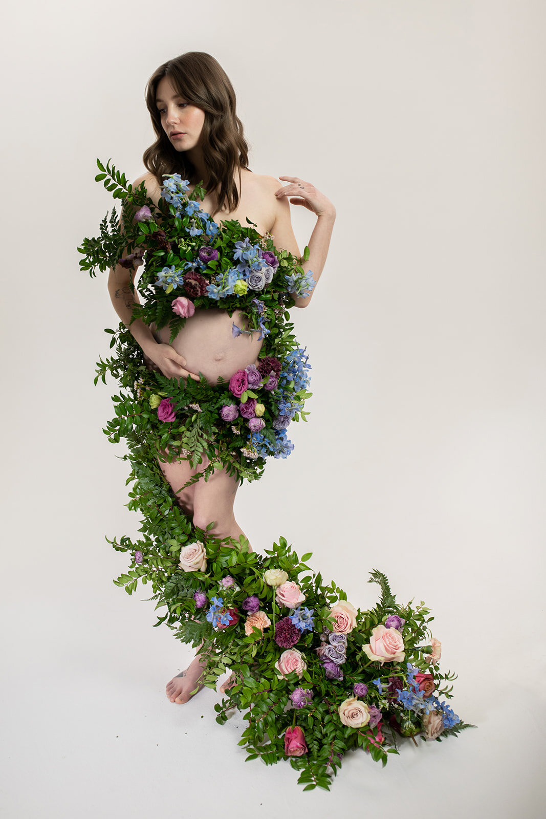Greek inspired maternity shoot with a wearable floral garland filled with blue delphinium, lavender spray roses, plum ranunculus, blush and fuchsia roses. Designed by wedding florist Rosemary & Finch in Nashville.