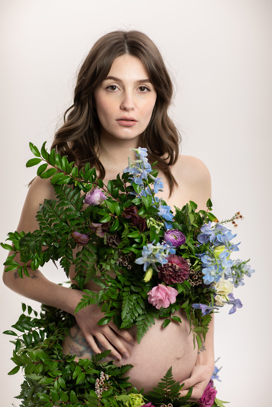 Greek inspired maternity shoot with a wearable floral garland filled with blue delphinium, lavender spray roses, plum ranunculus, blush and fuchsia roses. Designed by wedding florist Rosemary & Finch in Nashville.