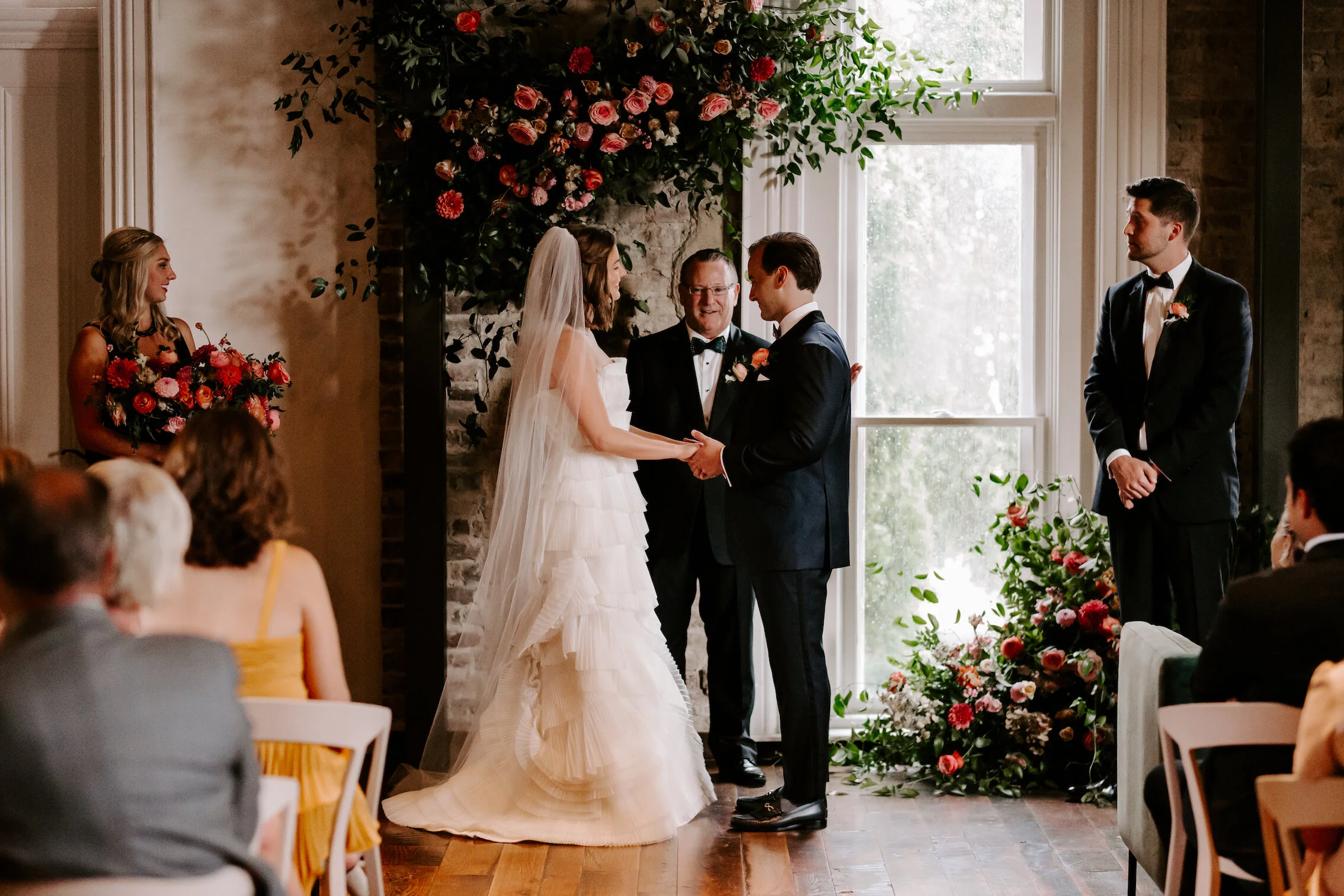 This wedding featured a stunning ceremony arch and a moss and floral wall installation. Blooms used were coral zinnias, fuchsia and blush dahlias, tangerine ranunculus, petal-heavy roses, pink snowberry, and sprawling smilax vine. Designed by Nashvi…