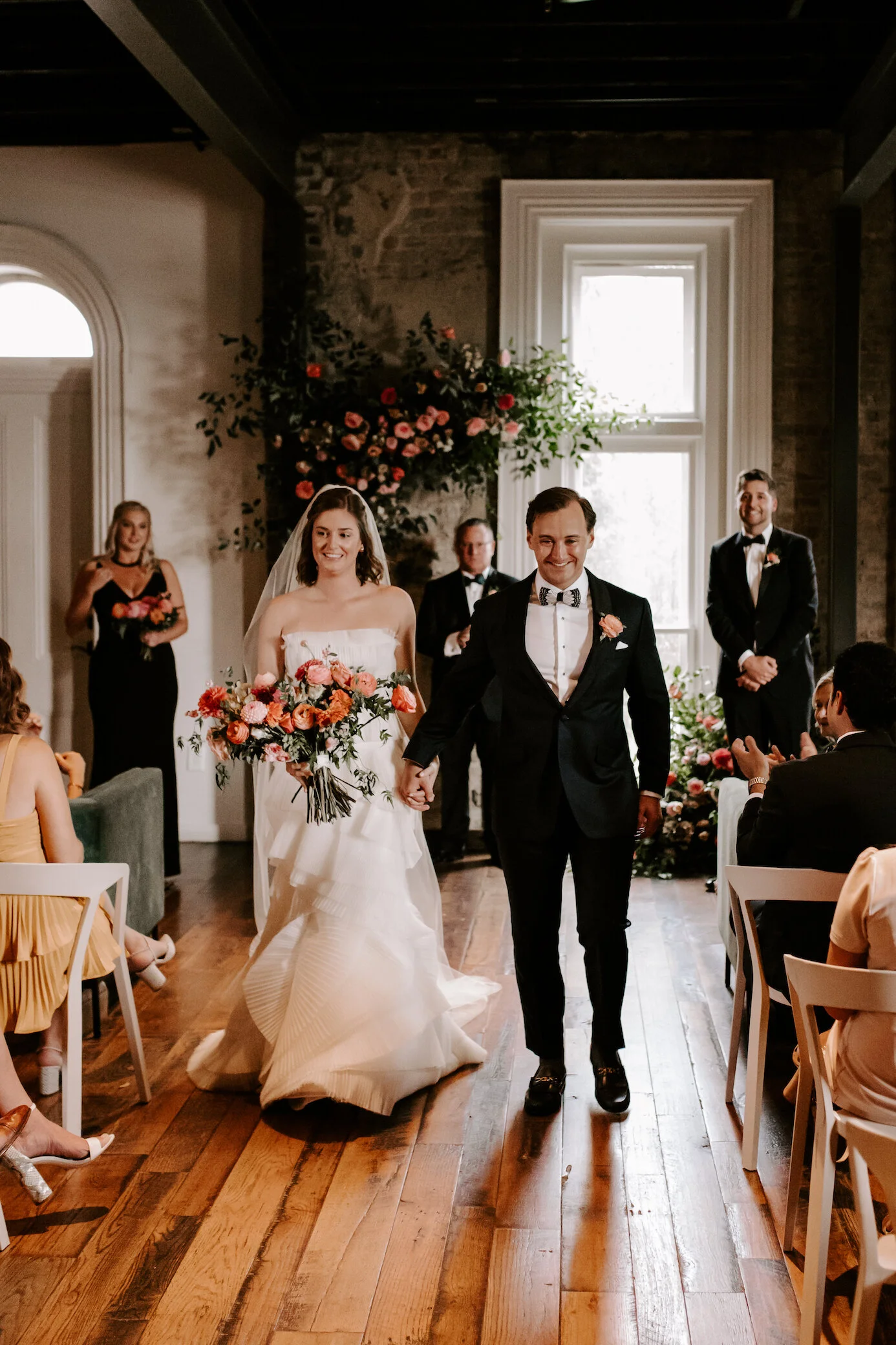 This wedding featured a stunning ceremony arch and a moss and floral wall installation. Blooms used were coral zinnias, fuchsia and blush dahlias, tangerine ranunculus, petal-heavy roses, pink snowberry, and sprawling smilax vine. Designed by Nashvi…